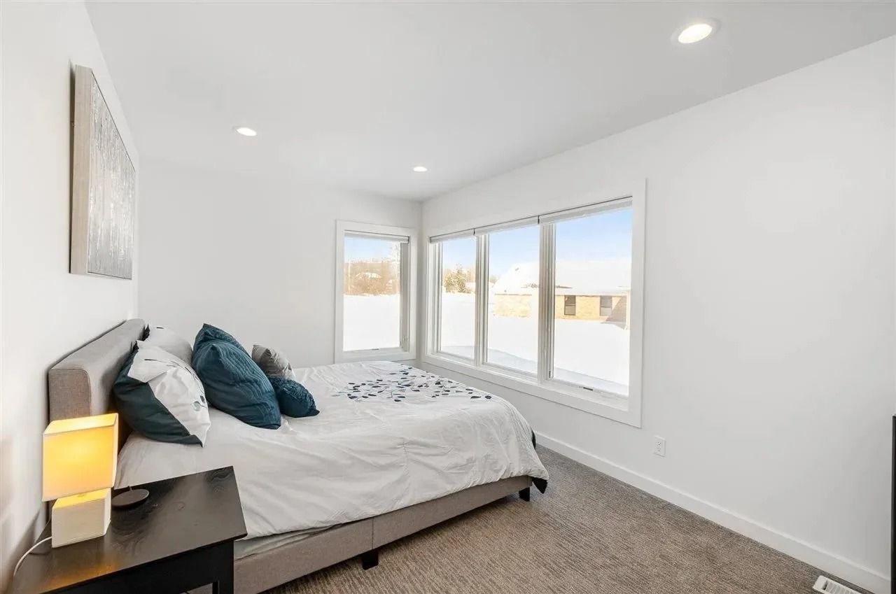 Bright bedroom with a bed, teal pillows, bedside lamp, and large corner windows