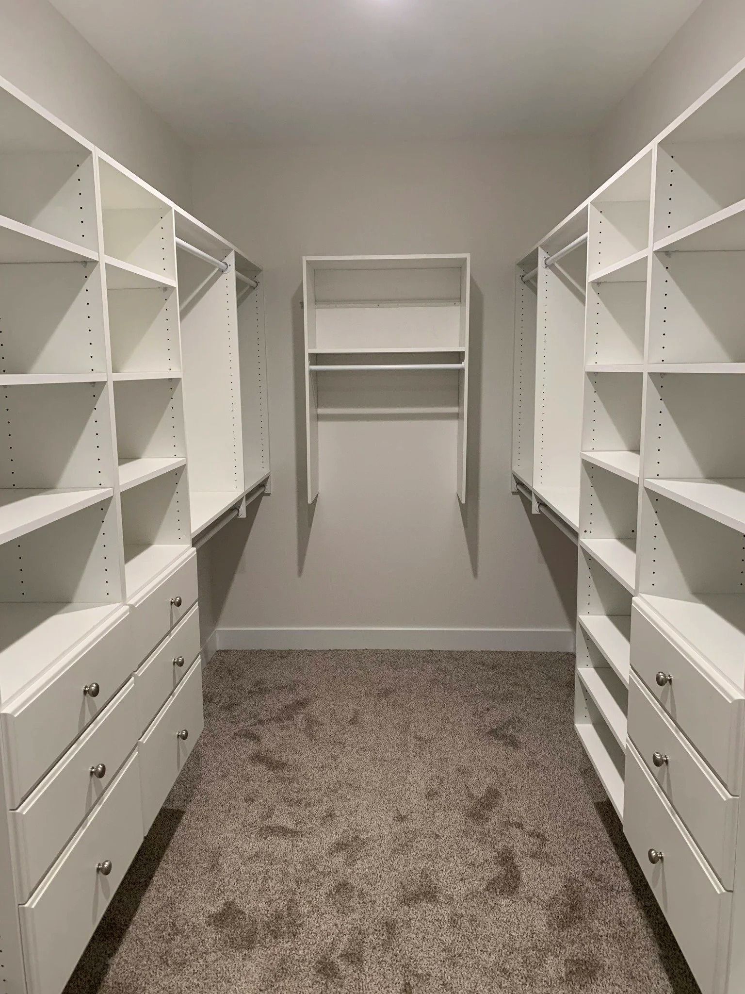 Empty walk-in closet with white shelving, drawers, and beige carpet.
