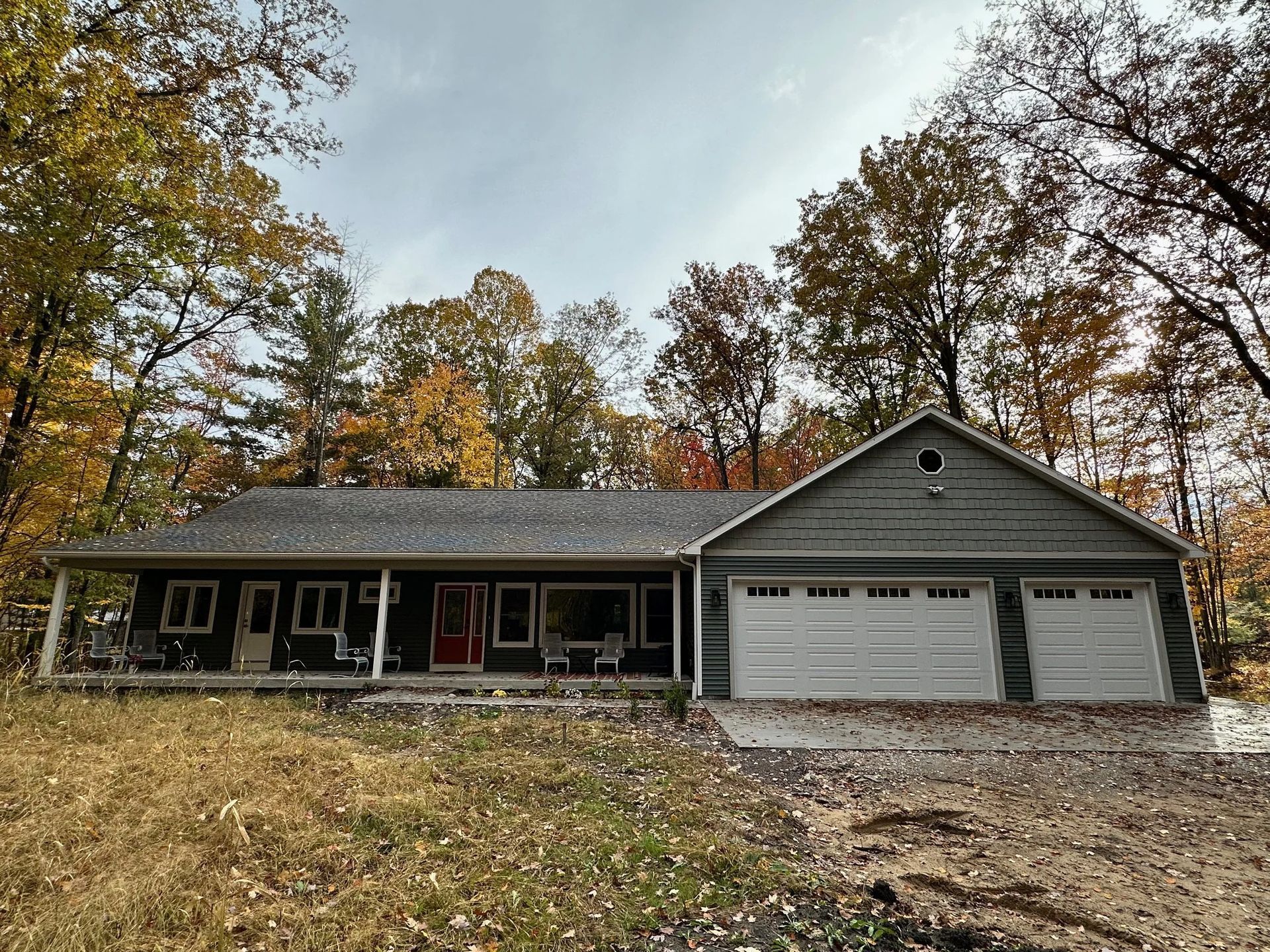 Single-story house with a two-car garage on a wooded hillside in autumn