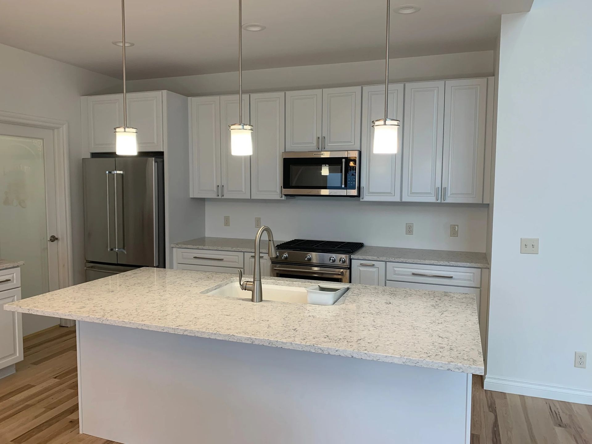 Modern white kitchen with island, stainless steel appliances, and pendant lights