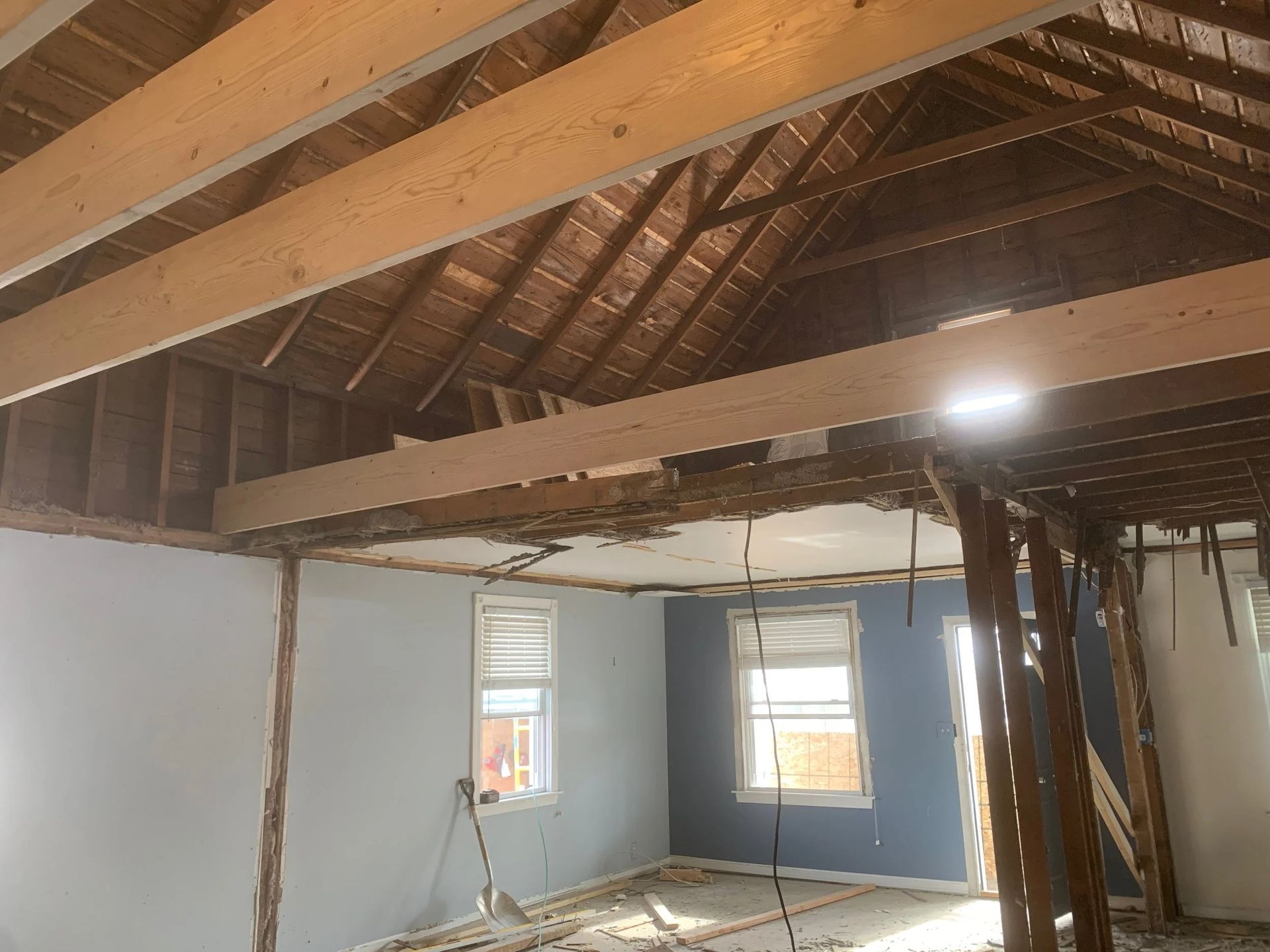 Damaged attic room with exposed beams, torn ceiling, and debris on the floor