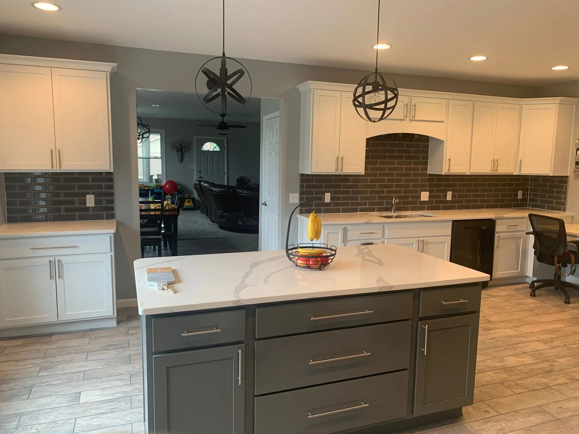 Modern kitchen with gray island, white cabinets, pendant lights, and bar stools beside a breakfast nook