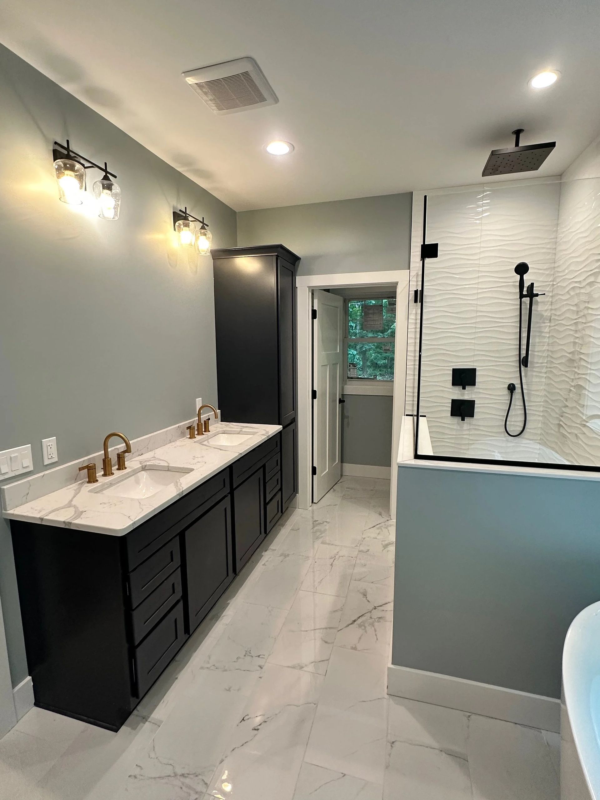 Modern bathroom with double vanity, large mirror lights, white tile shower, and black cabinetry
