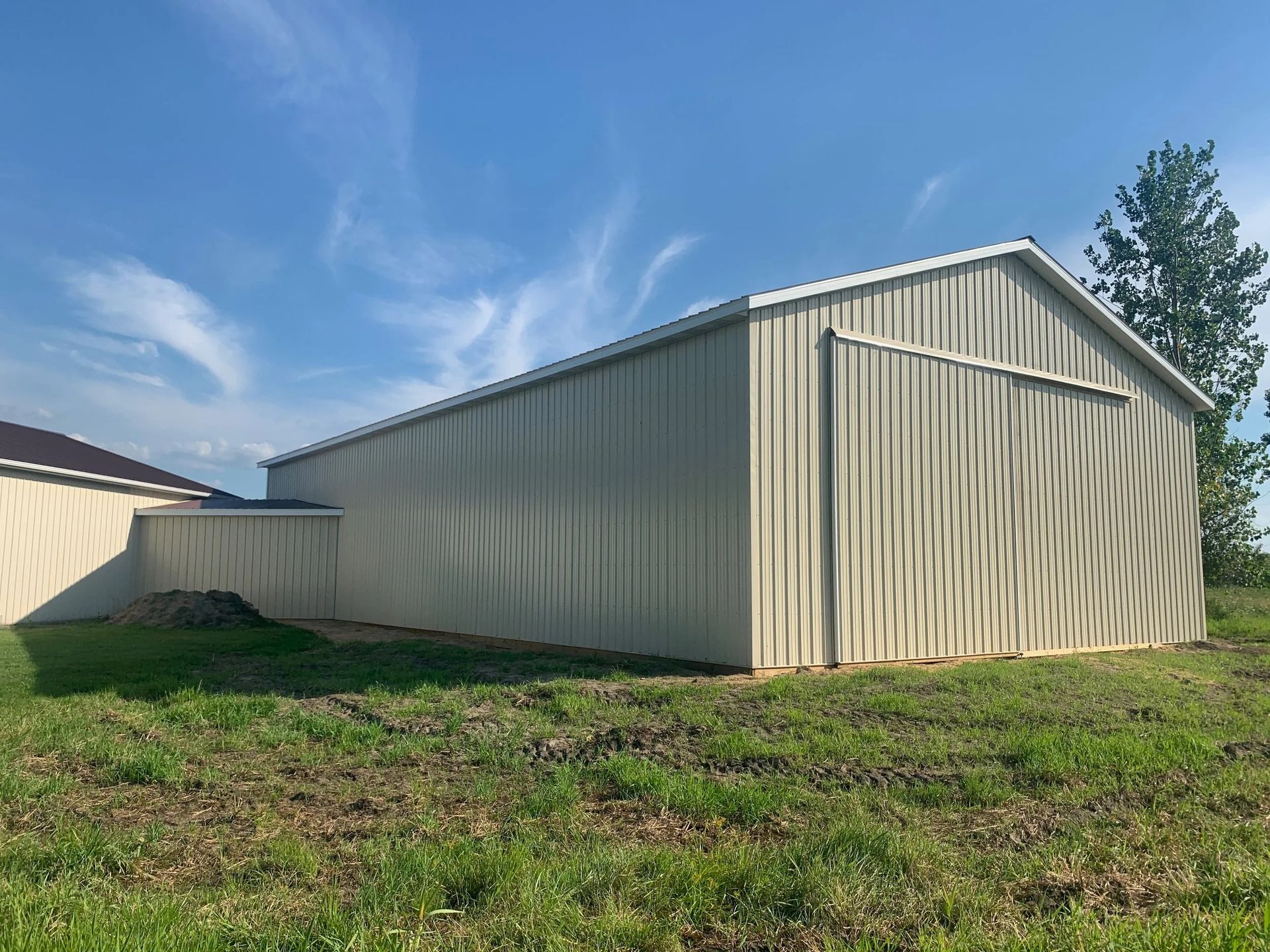Beige metal shed in a grassy yard under a blue sky with wispy clouds