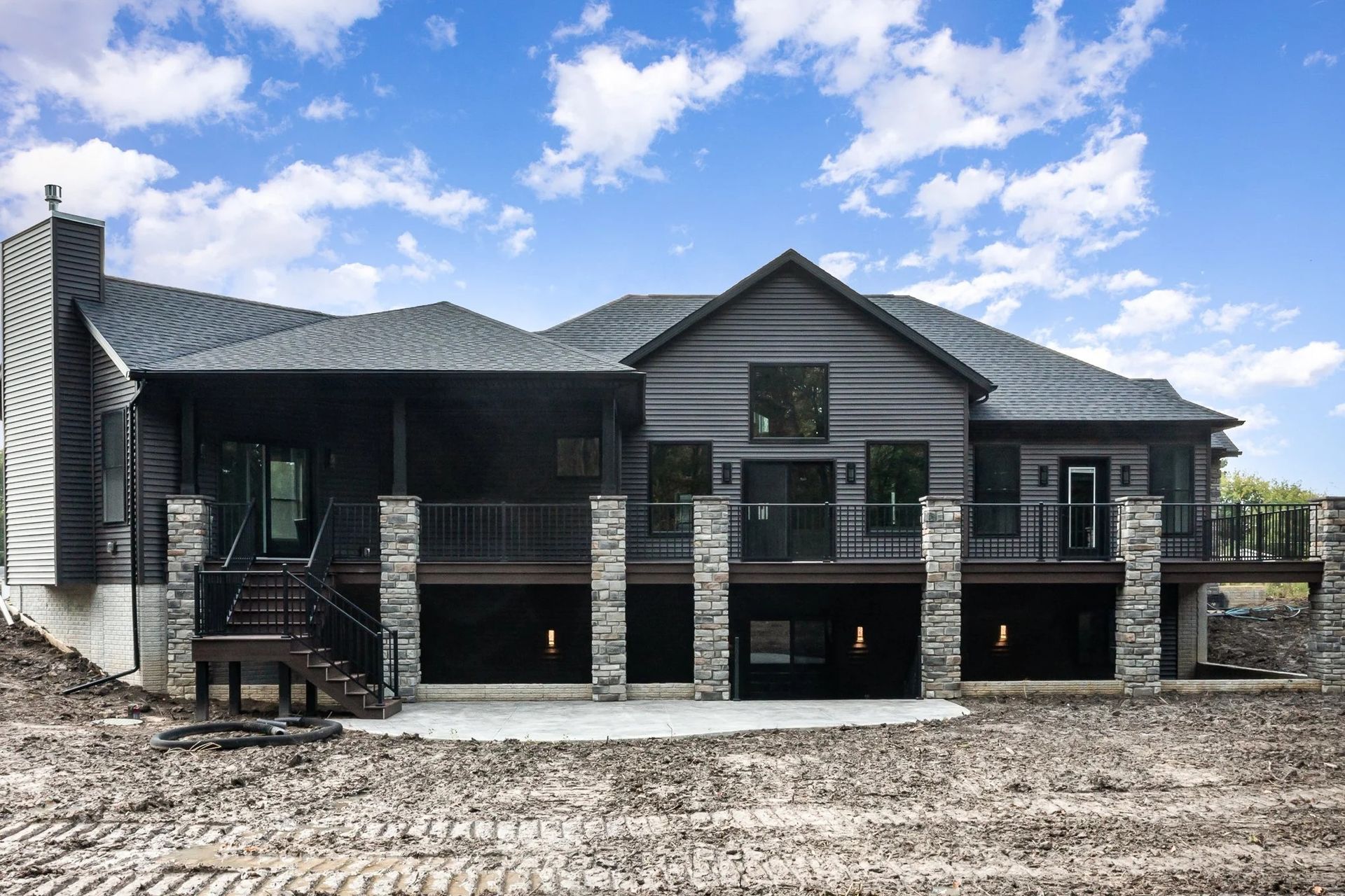 Large modern dark-gray house under construction with stone accents and a muddy front yard