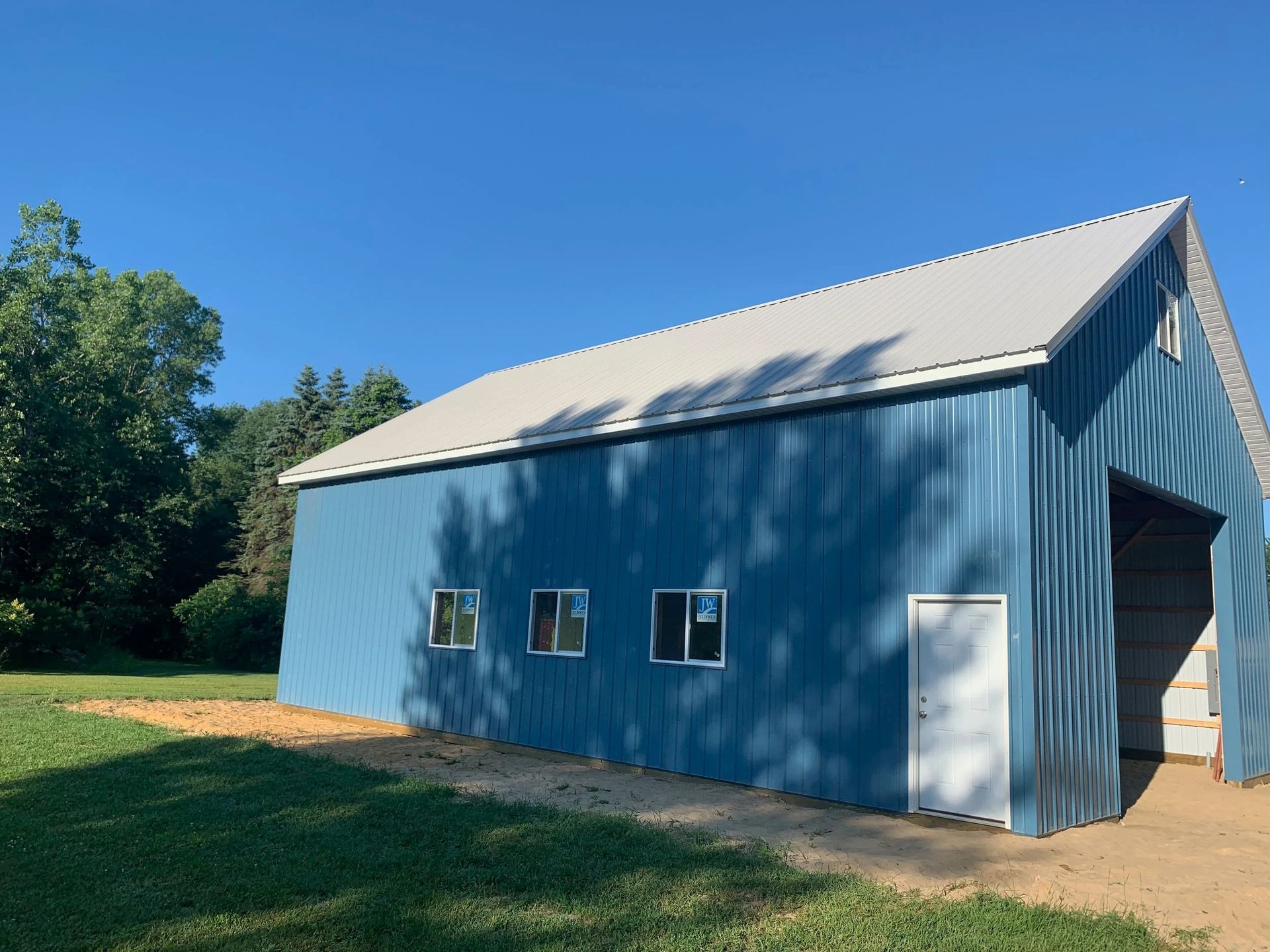 Blue barn-like building with a white roof and doors on a sunny grassy lot