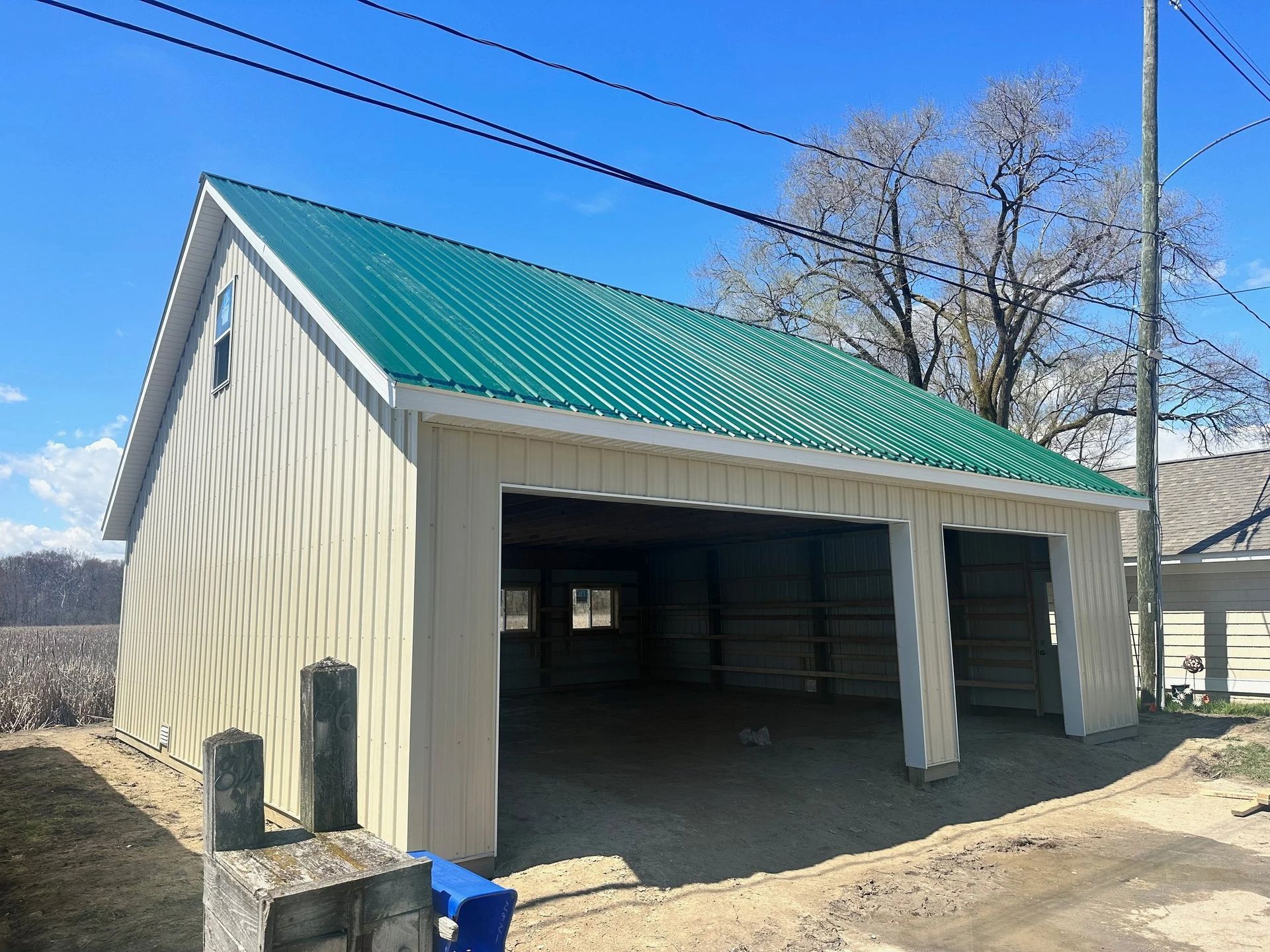 Small beige garage with green metal roof and open bays on a rural roadside.