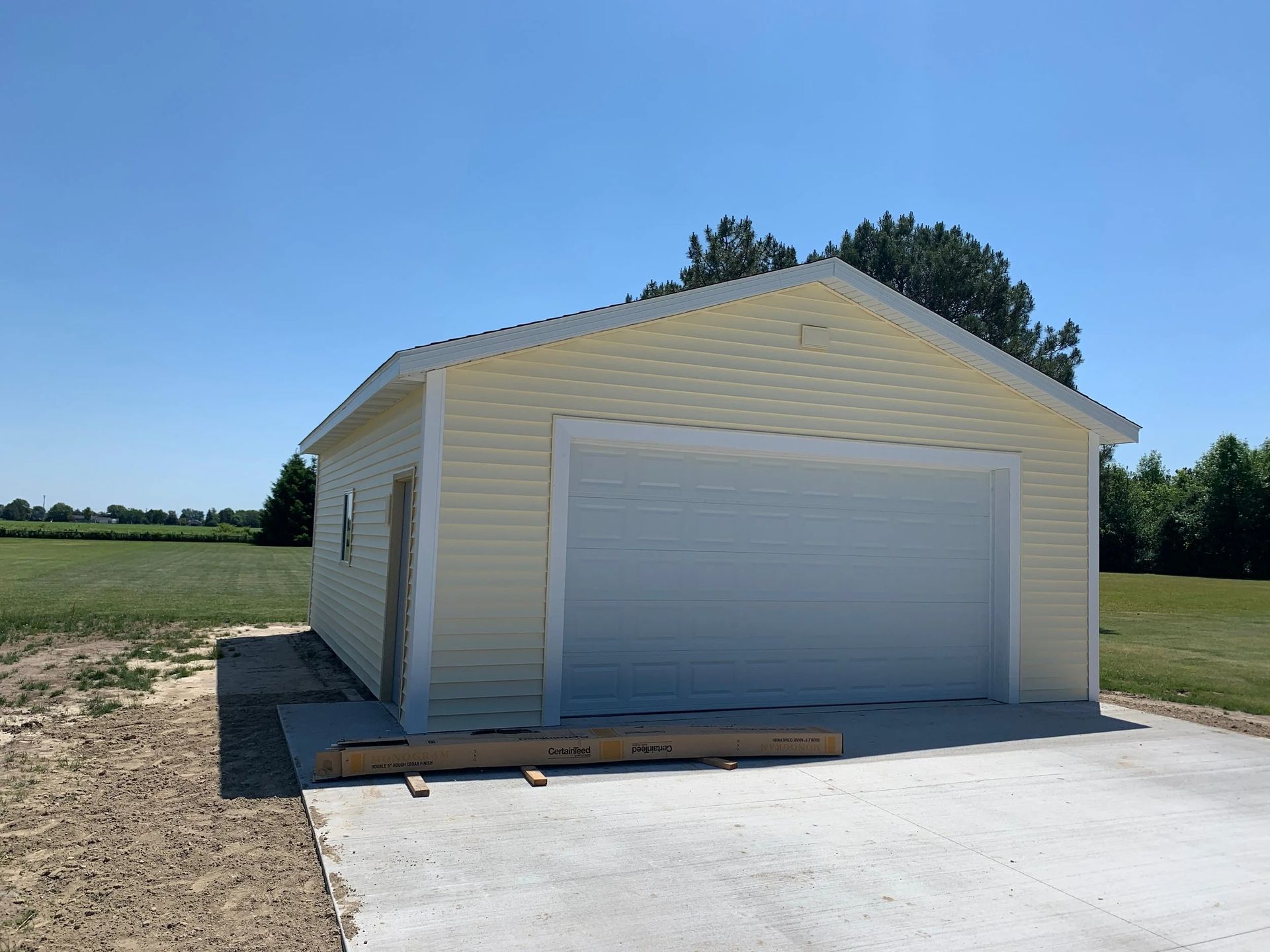 Detached beige garage with a white roll-up door beside a concrete driveway under a clear sky