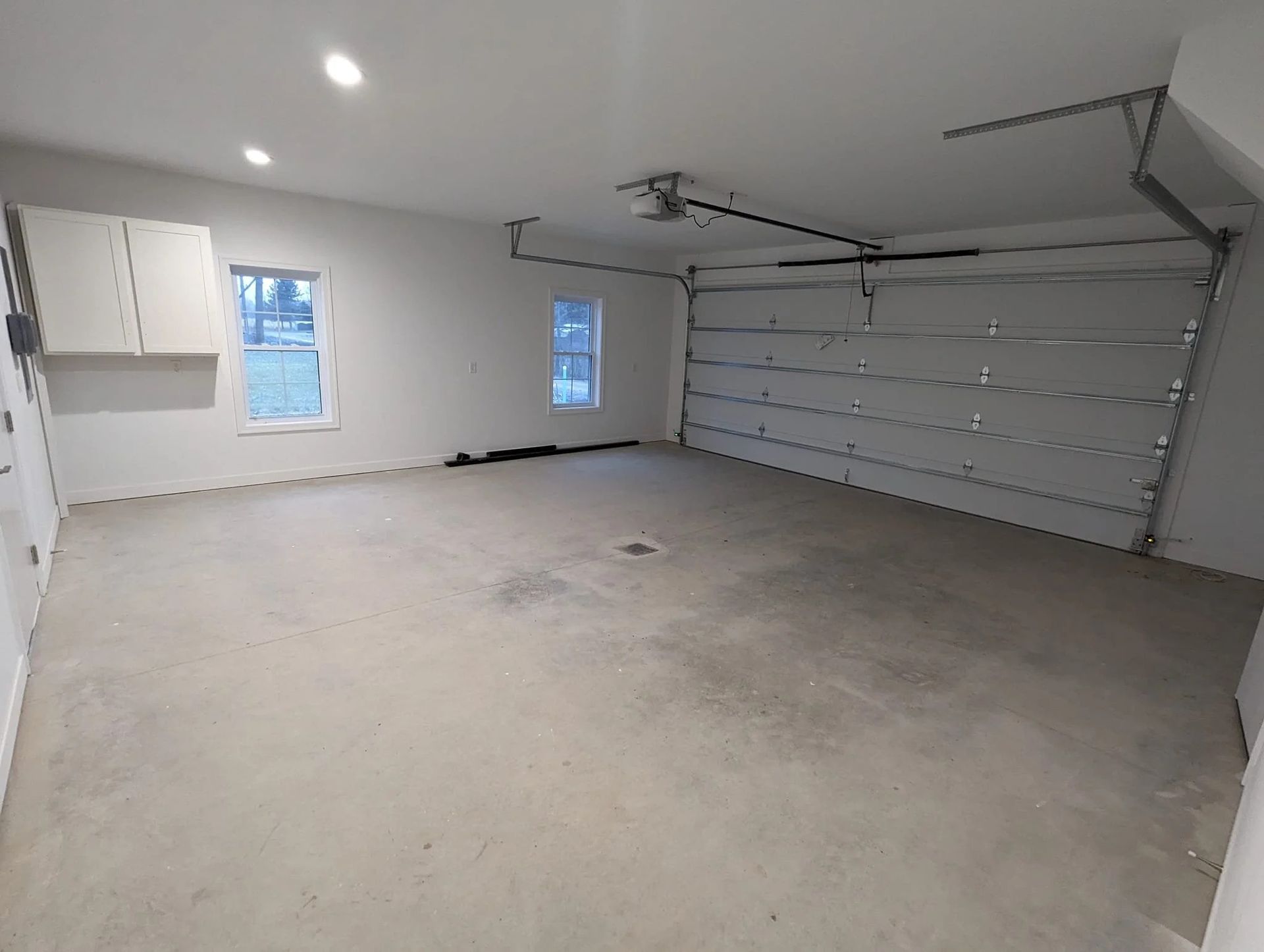 Empty two-car garage with white walls, concrete floor, small windows, and closed garage doors.
