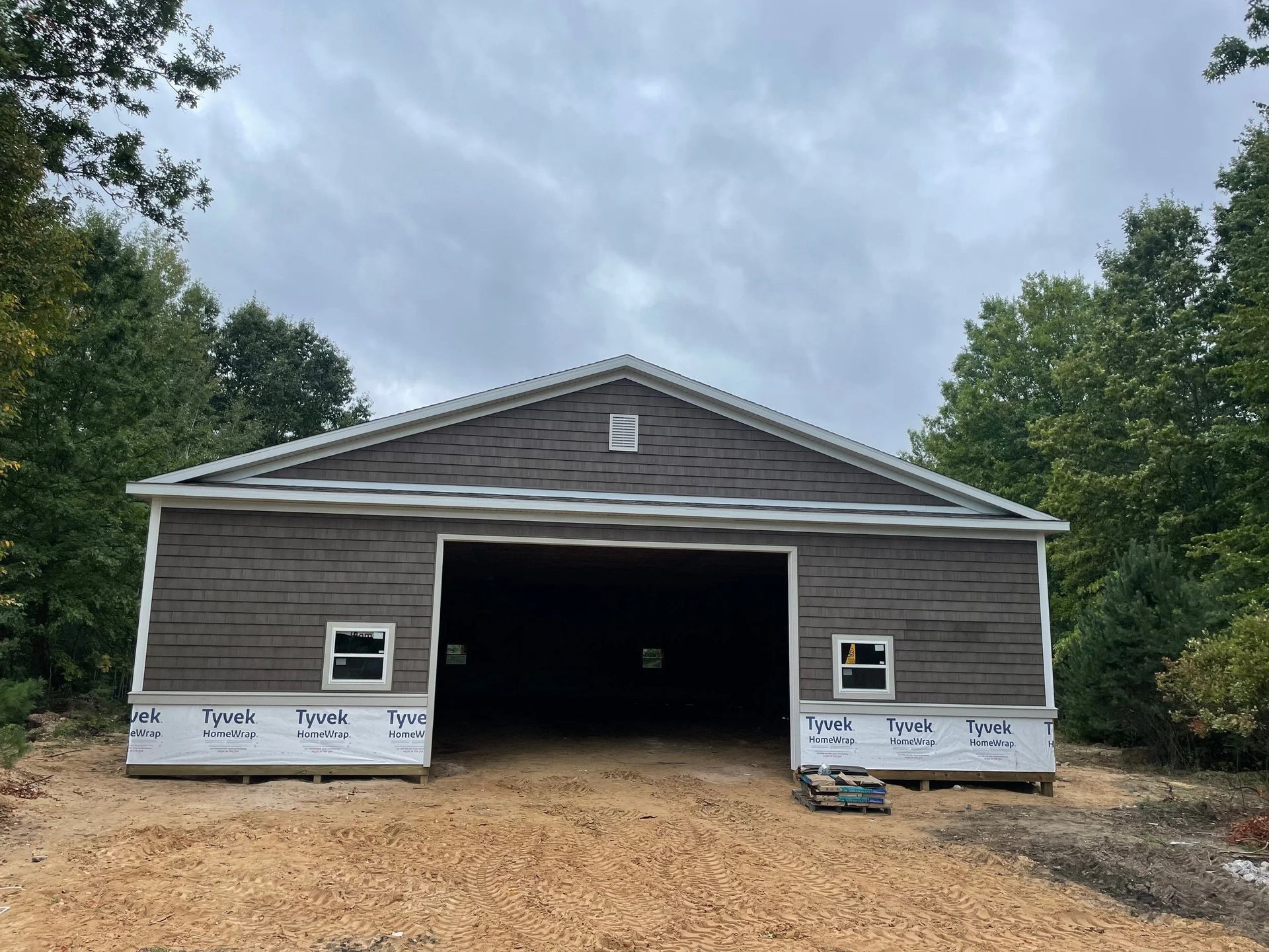 Unfinished single-story garage with open center bay, gray siding, and white trim under a cloudy sky