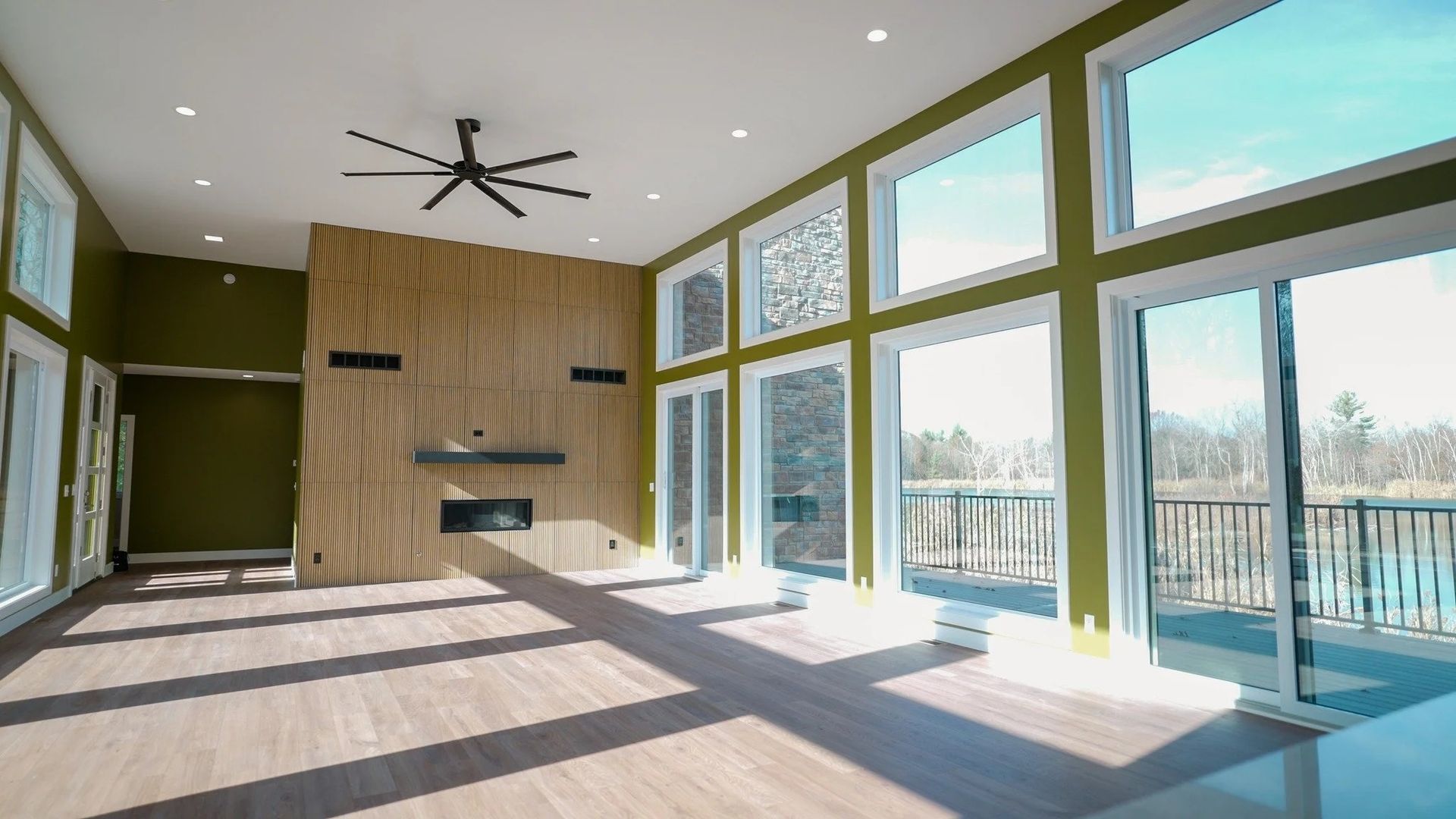 Bright modern living room with large windows, wood accent wall, ceiling fan, and sunlight on the floor