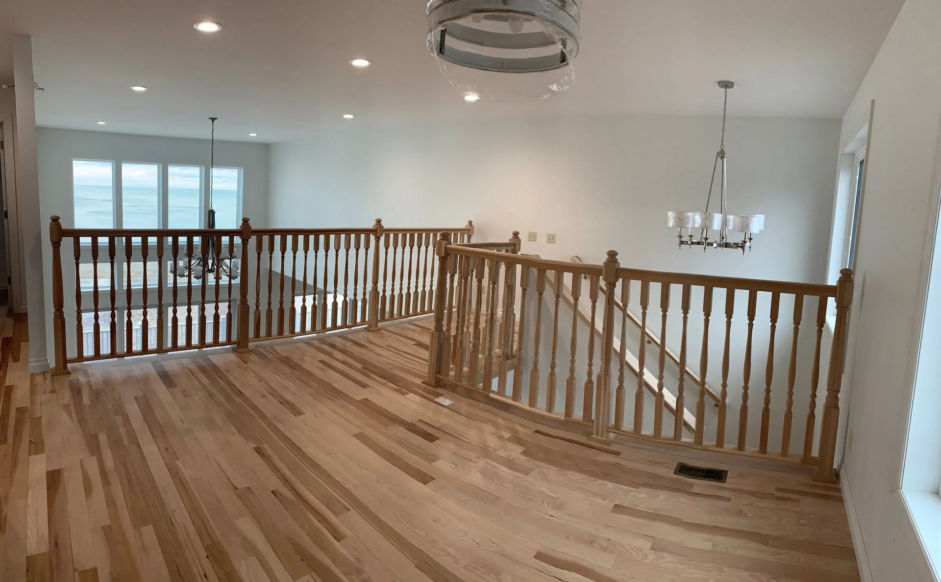Spacious hardwood loft with wooden railing, chandelier, and large windows overlooking the lower level