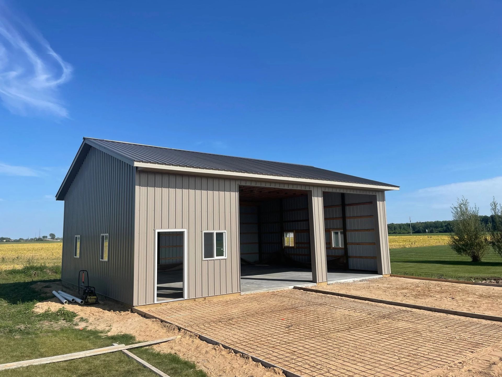 Small tan metal barn with open garage bay on a dirt lot under a blue sky