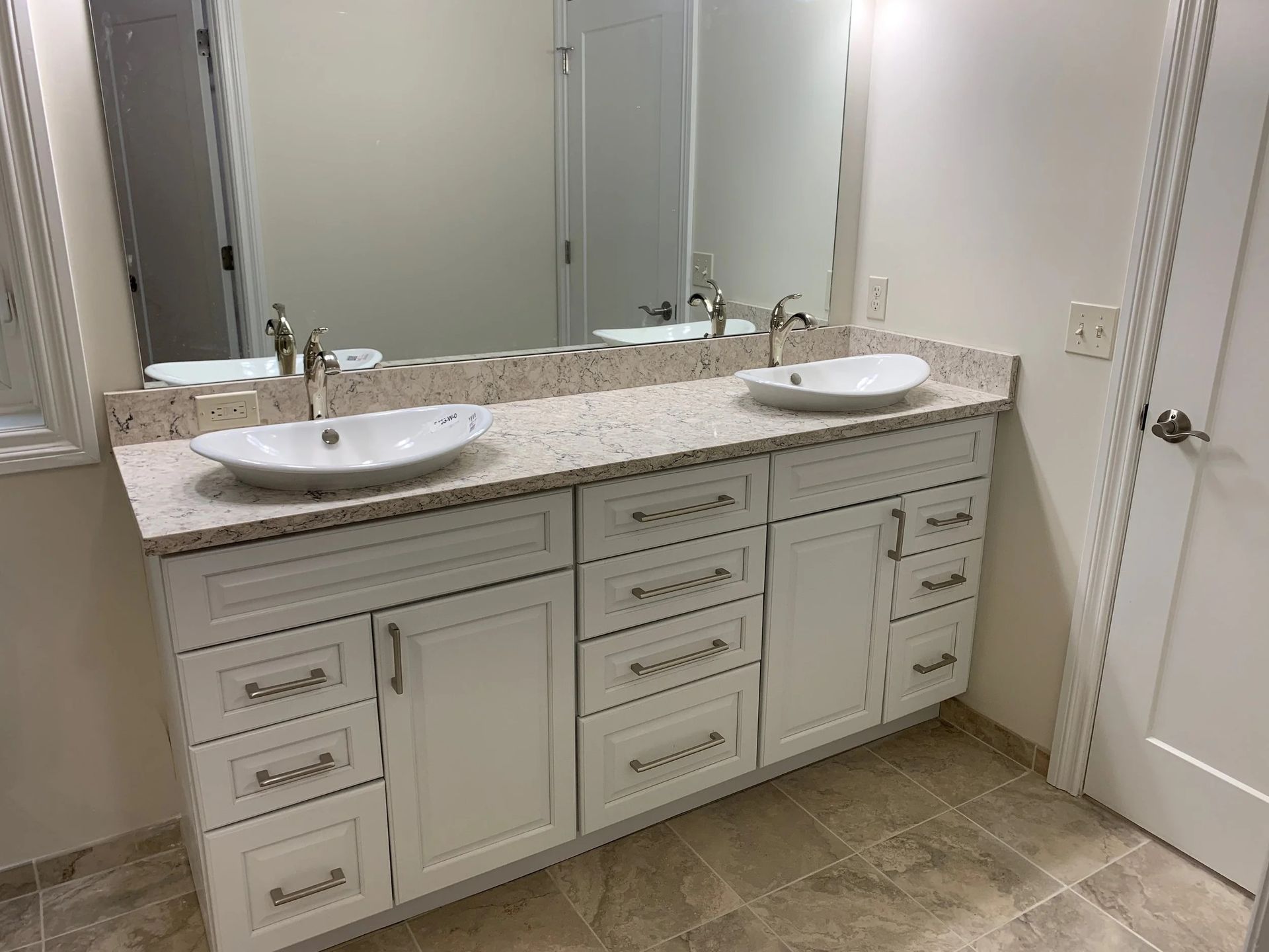 Double-sink bathroom vanity with granite countertop, mirrors, and white cabinets on beige tile floor