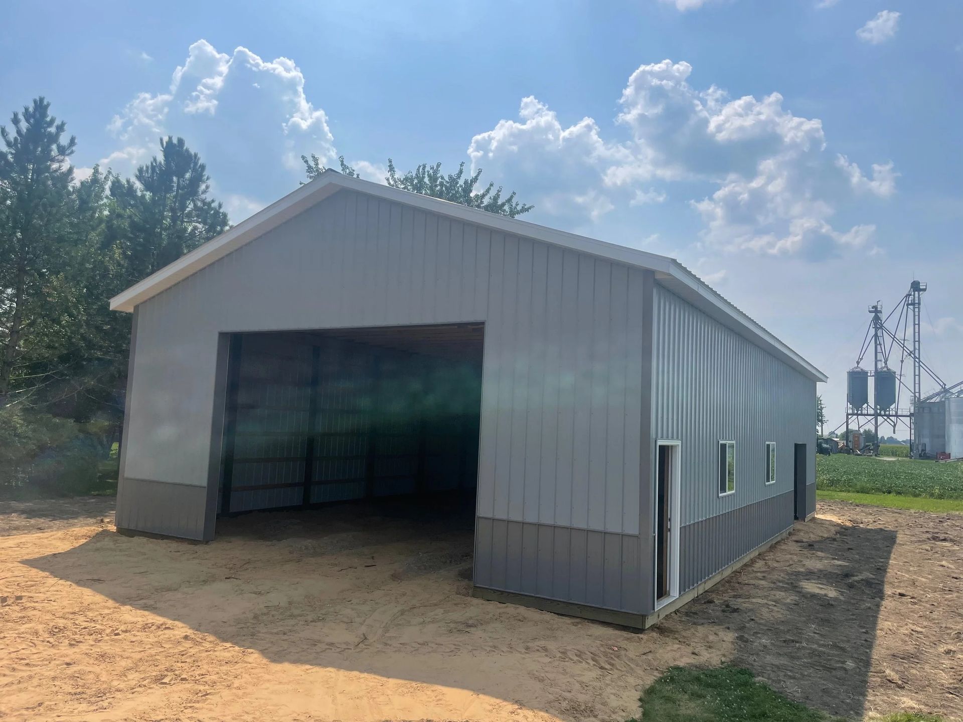 Gray metal barn with open front on a dirt lot under a sunny sky