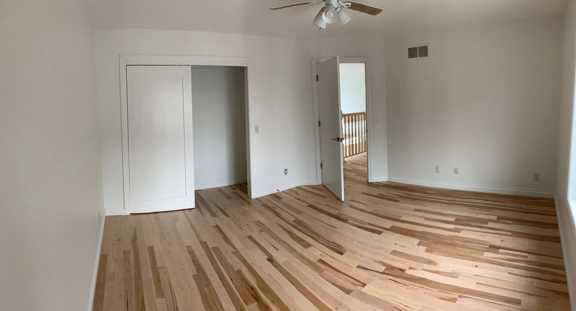 Empty white room with hardwood floor, ceiling fan, and doorway to a hallway