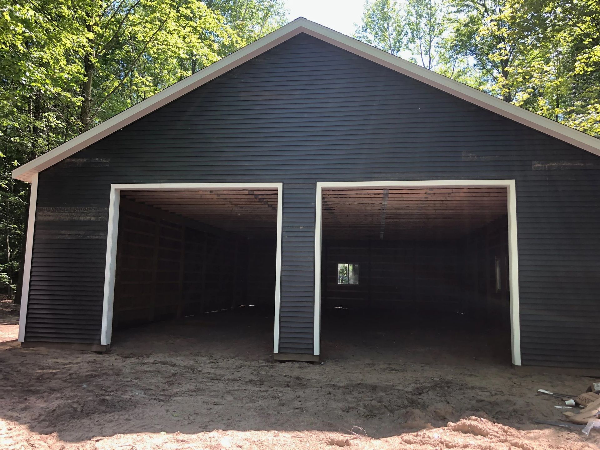 Black two-bay garage with open doors on a dirt lot, surrounded by trees