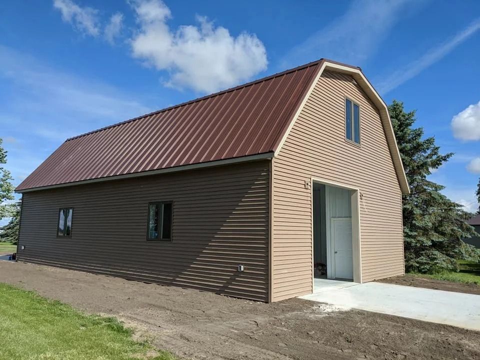 Brown barn-style shed with a red roof, white garage door, and small windows under a blue sky