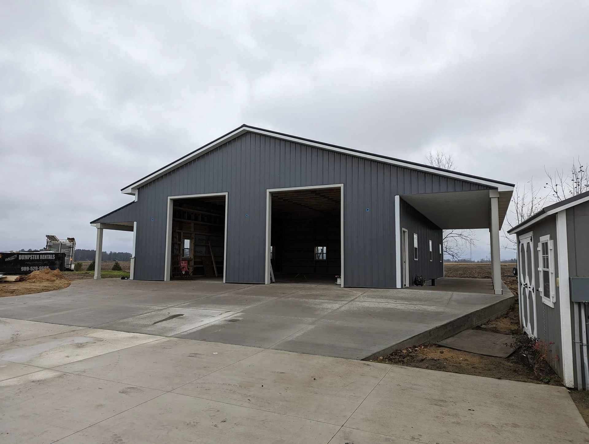 Gray metal warehouse with open bays on a concrete lot under an overcast sky