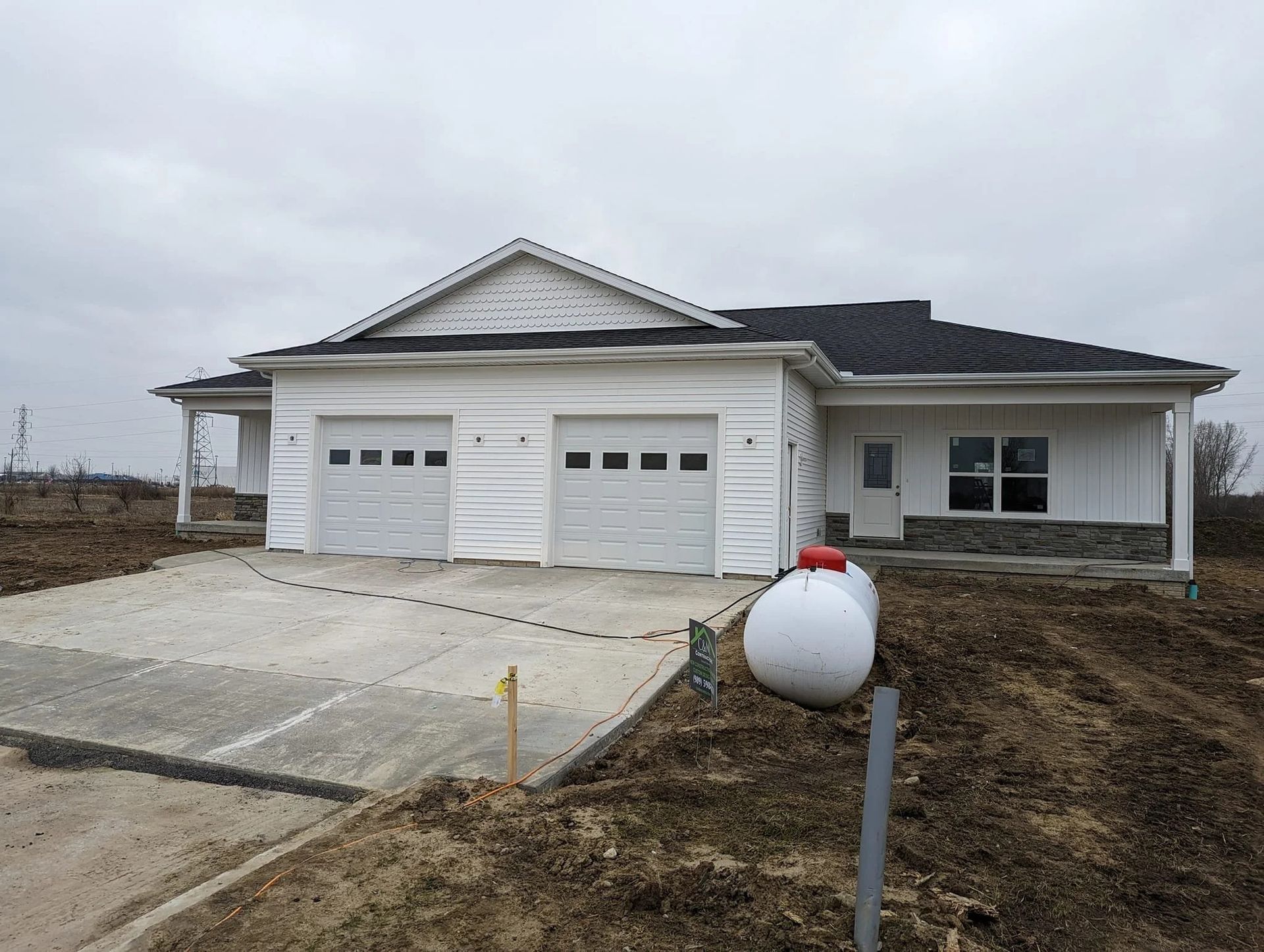 New single-story house with white garage doors and a concrete driveway under construction