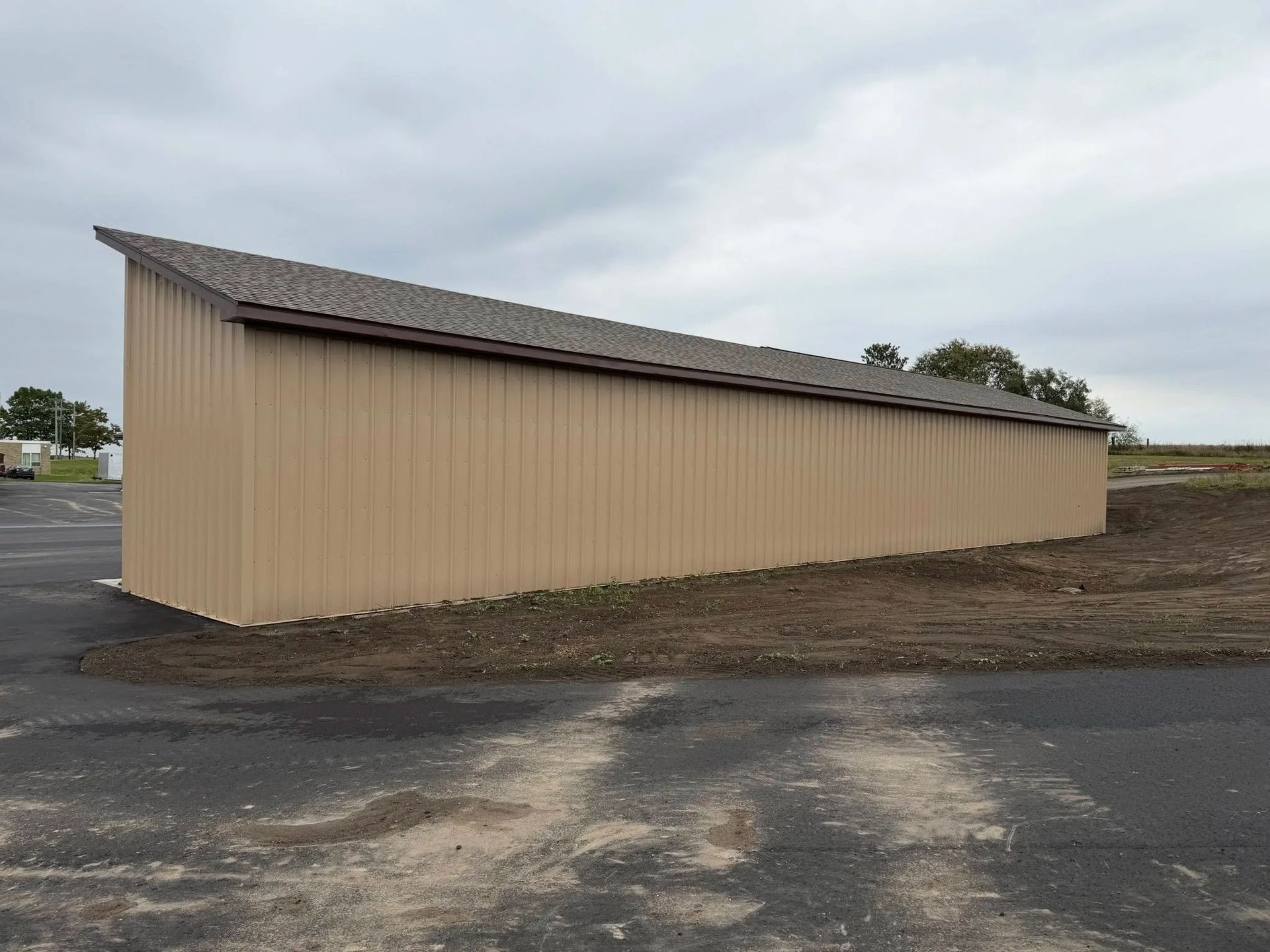 Beige metal storage building with a sloped roof on a gravel lot under an overcast sky