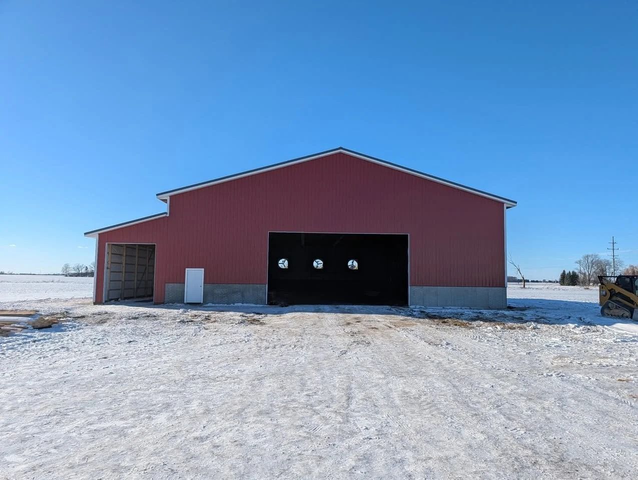 Red barn with open garage doors on a snowy rural lot under a clear blue sky