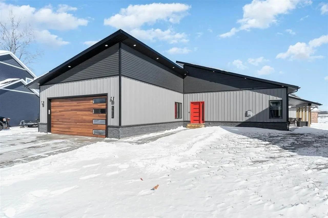 Modern gray house with black roof and wood garage door in a snowy landscape under a blue sky