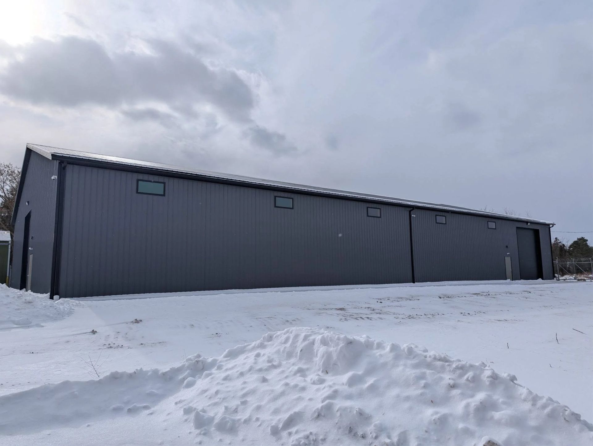 Long gray metal warehouse on a snowy field under an overcast sky