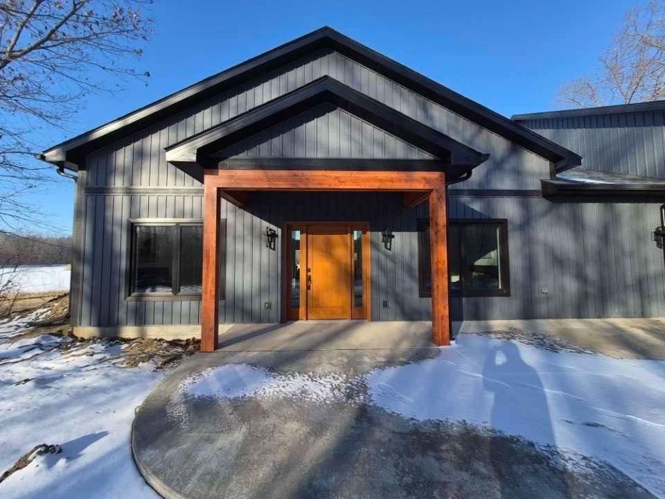 Snowy front entrance of a dark gray house with wood-framed porch and orange door