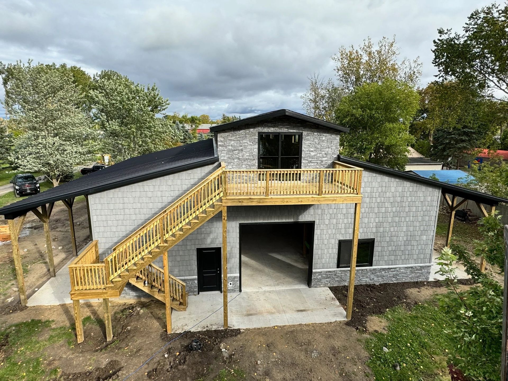 Two-story gray house with yellow exterior stairs and balcony under construction, surrounded by trees.
