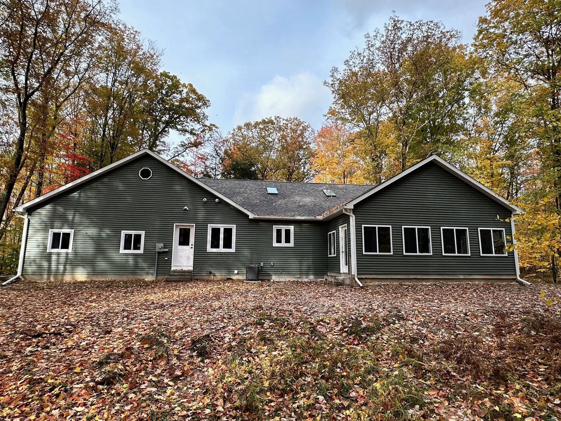 Gray house with black roof in autumn woods, covered by fallen leaves under a cloudy sky