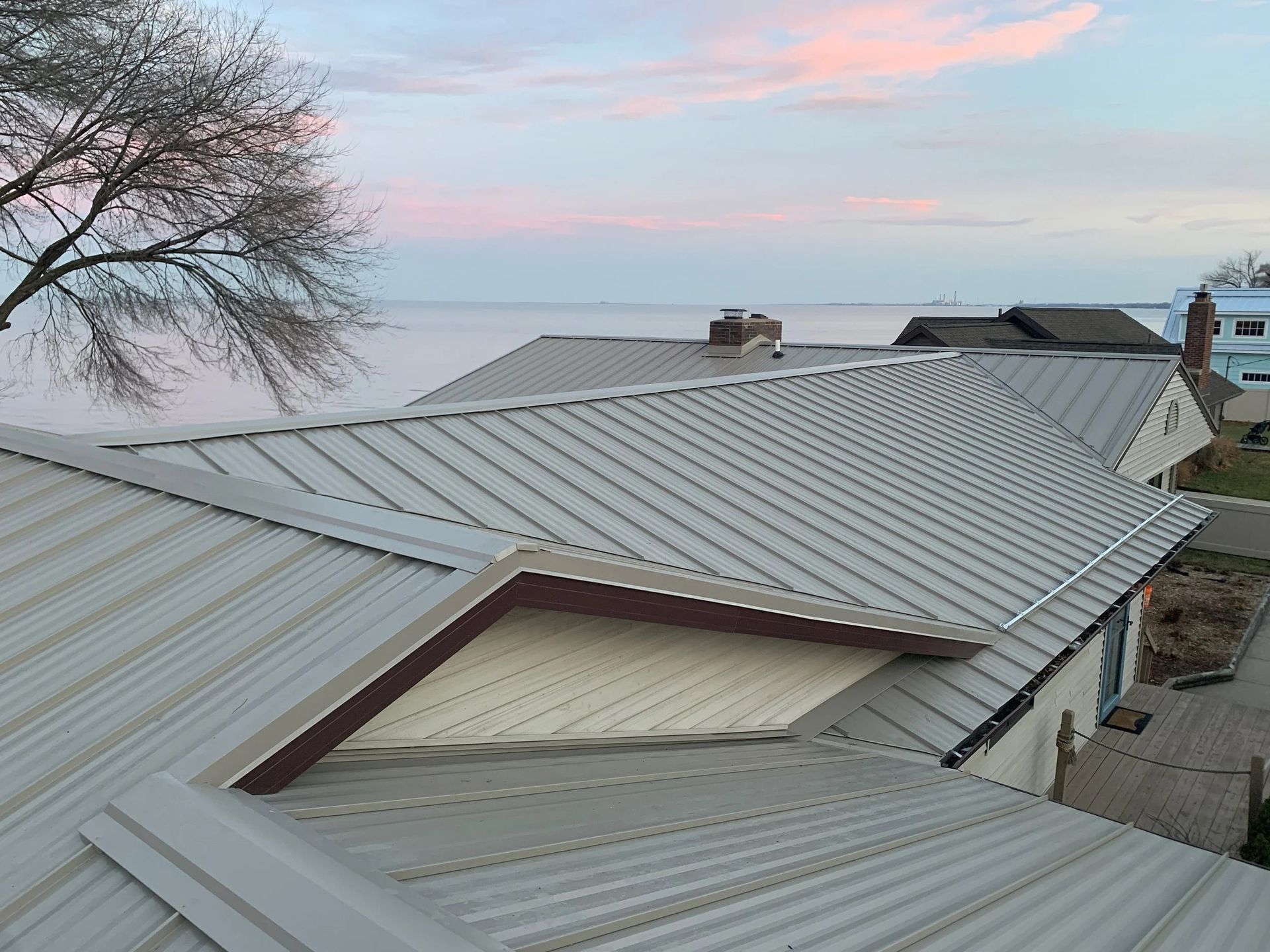 Rooftops with light gray metal roofing under a pink sunset sky by the water