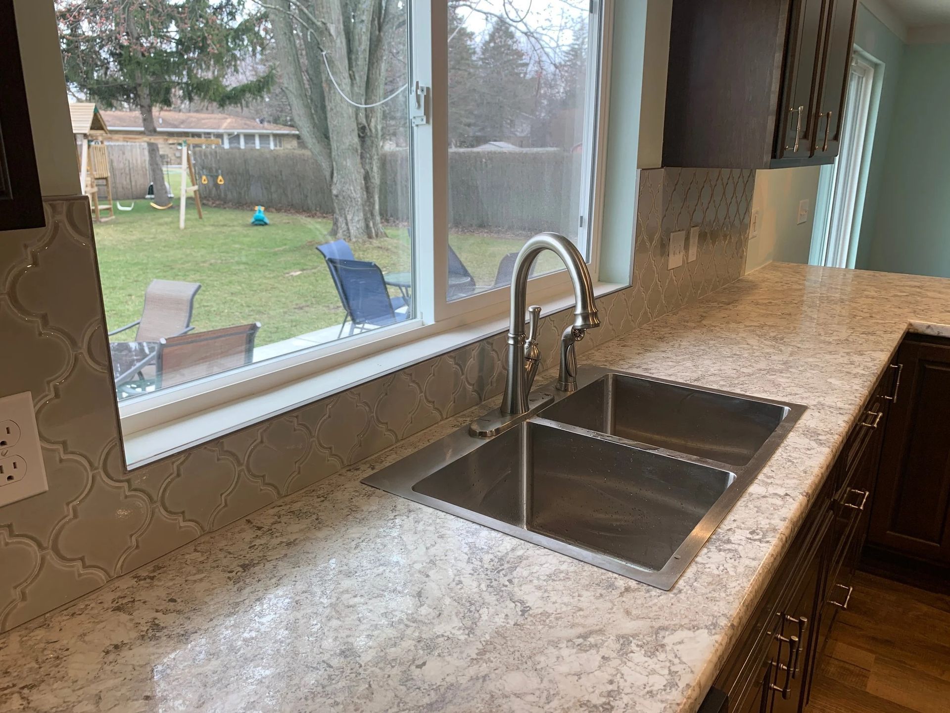 Modern kitchen countertop with double sink and large window overlooking a backyard