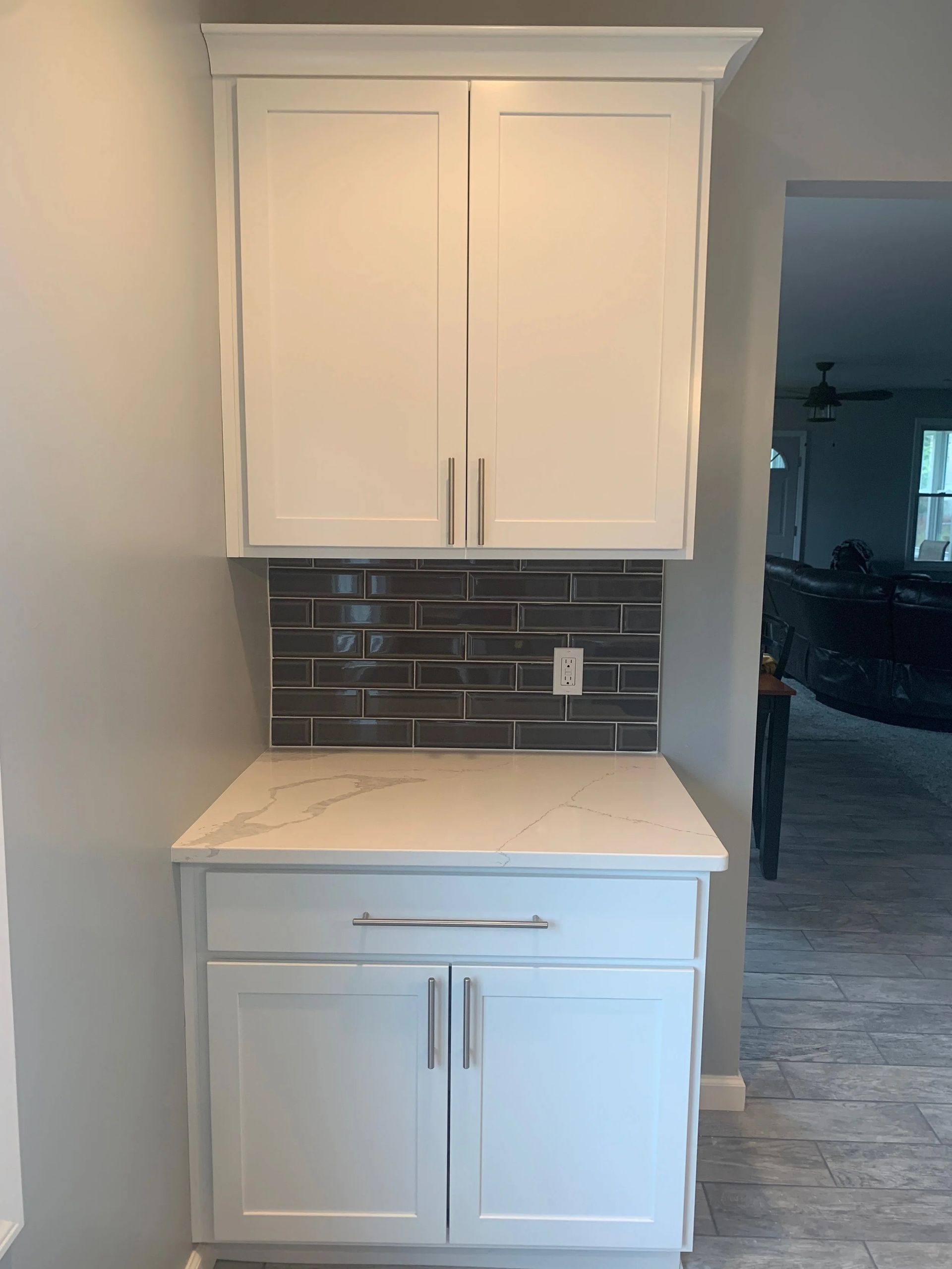 White cabinet with marble countertop and dark tile backsplash in a kitchen alcove