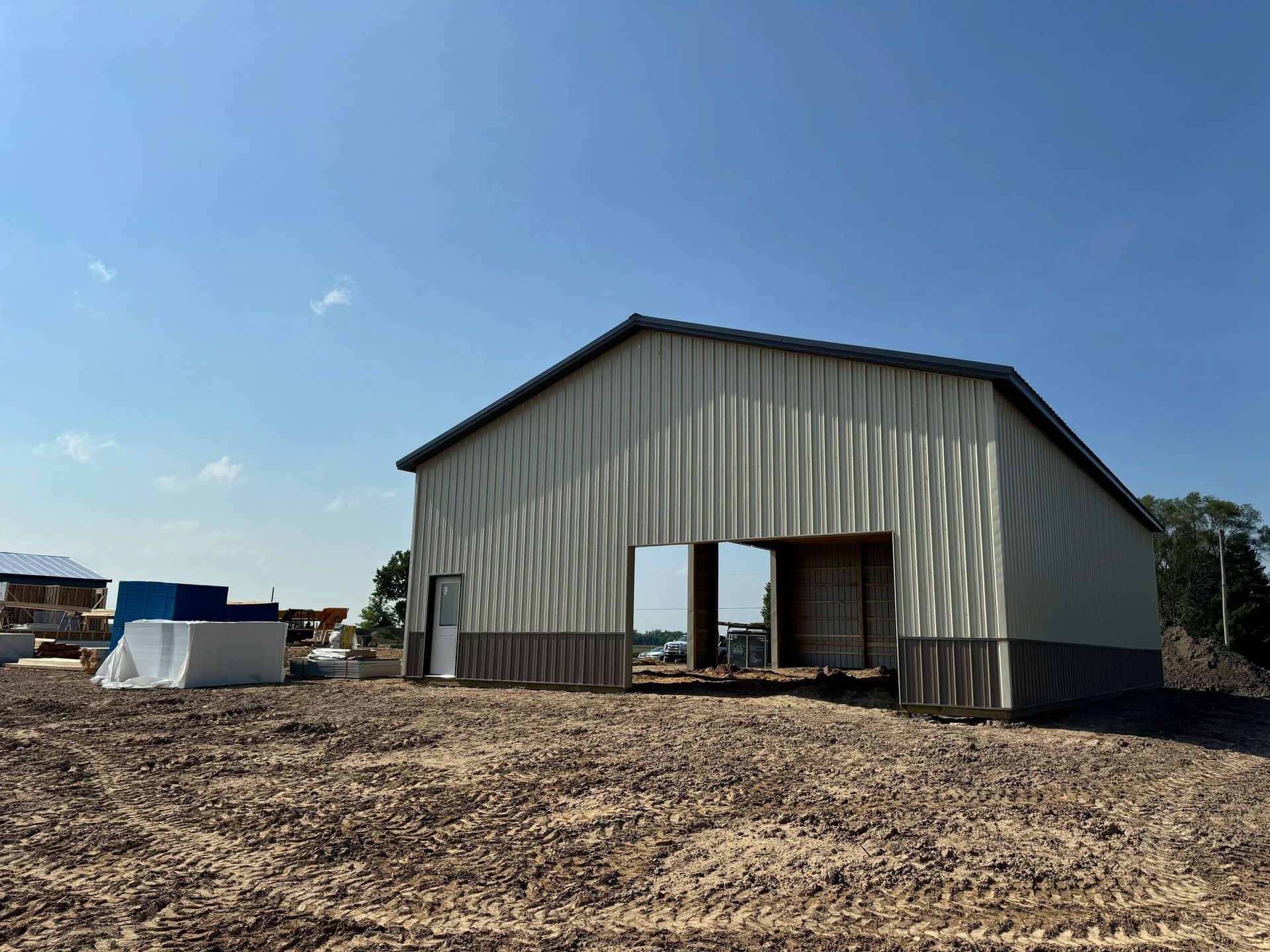Large metal barn under blue sky, with open doorway and dirt ground in front