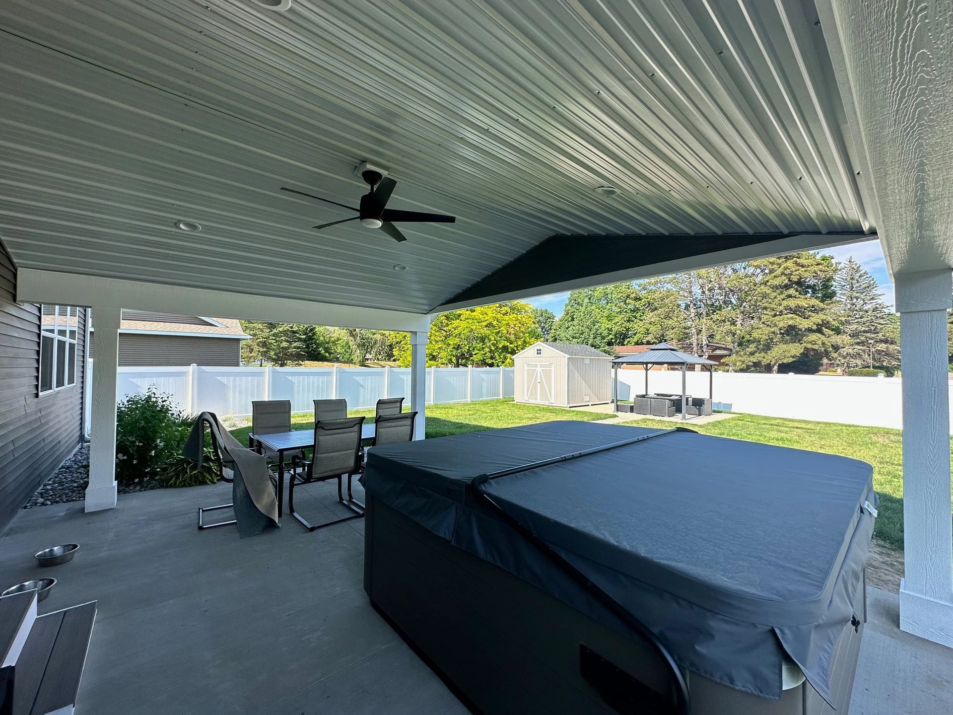 Covered patio with outdoor dining set, hot tub, ceiling fan, and backyard lawn in bright daylight
