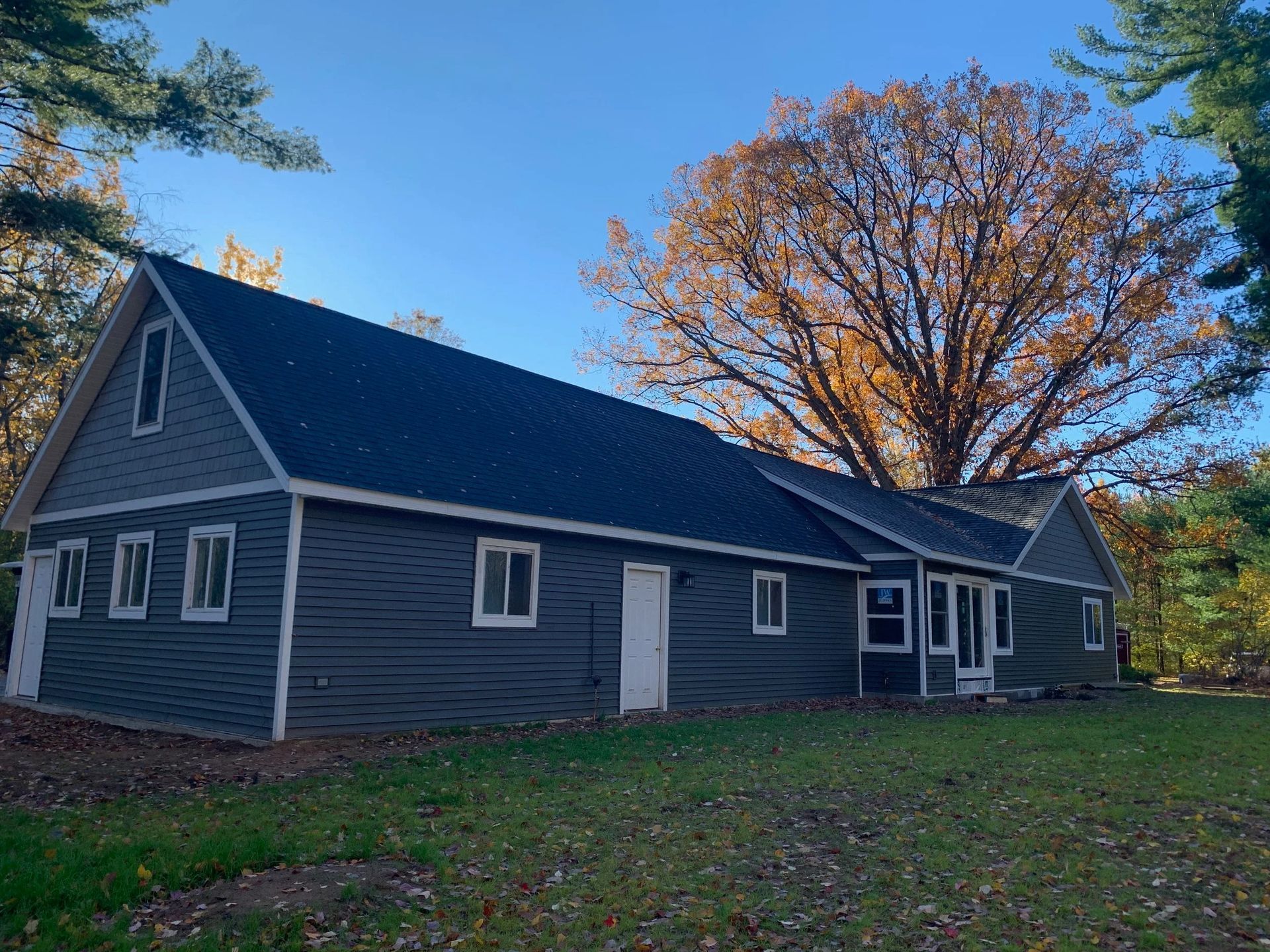 Gray house with white trim and a sloped roof, surrounded by trees in autumn.