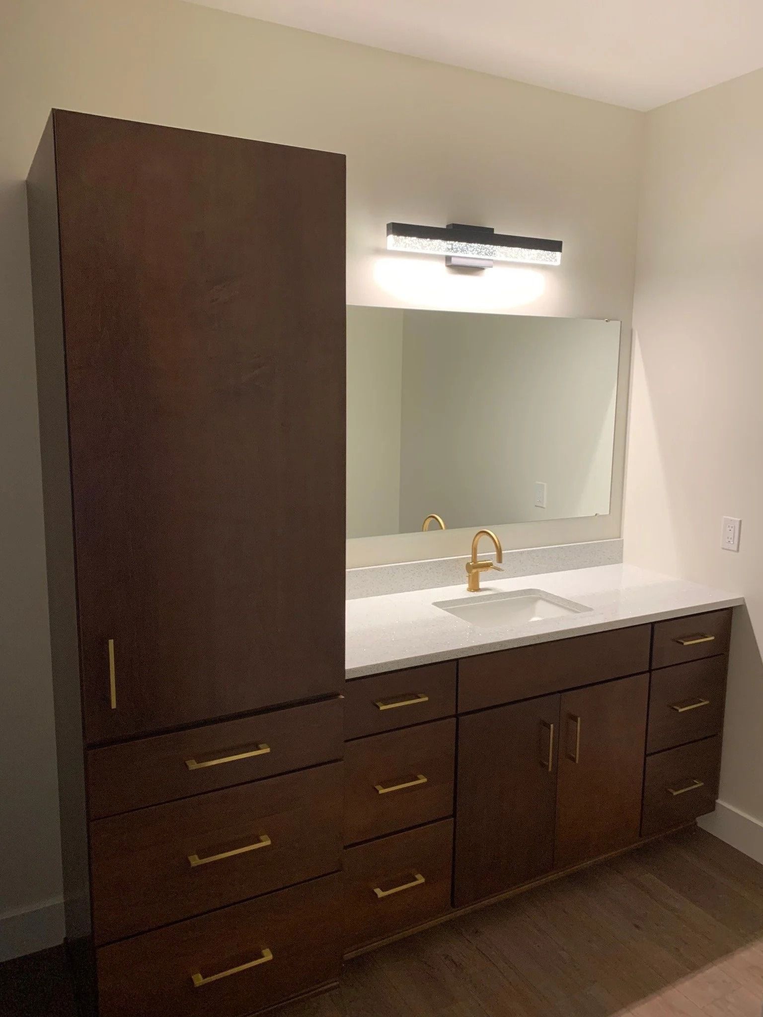 Modern bathroom vanity with dark wood cabinets, large mirror, and wall-mounted light fixture.