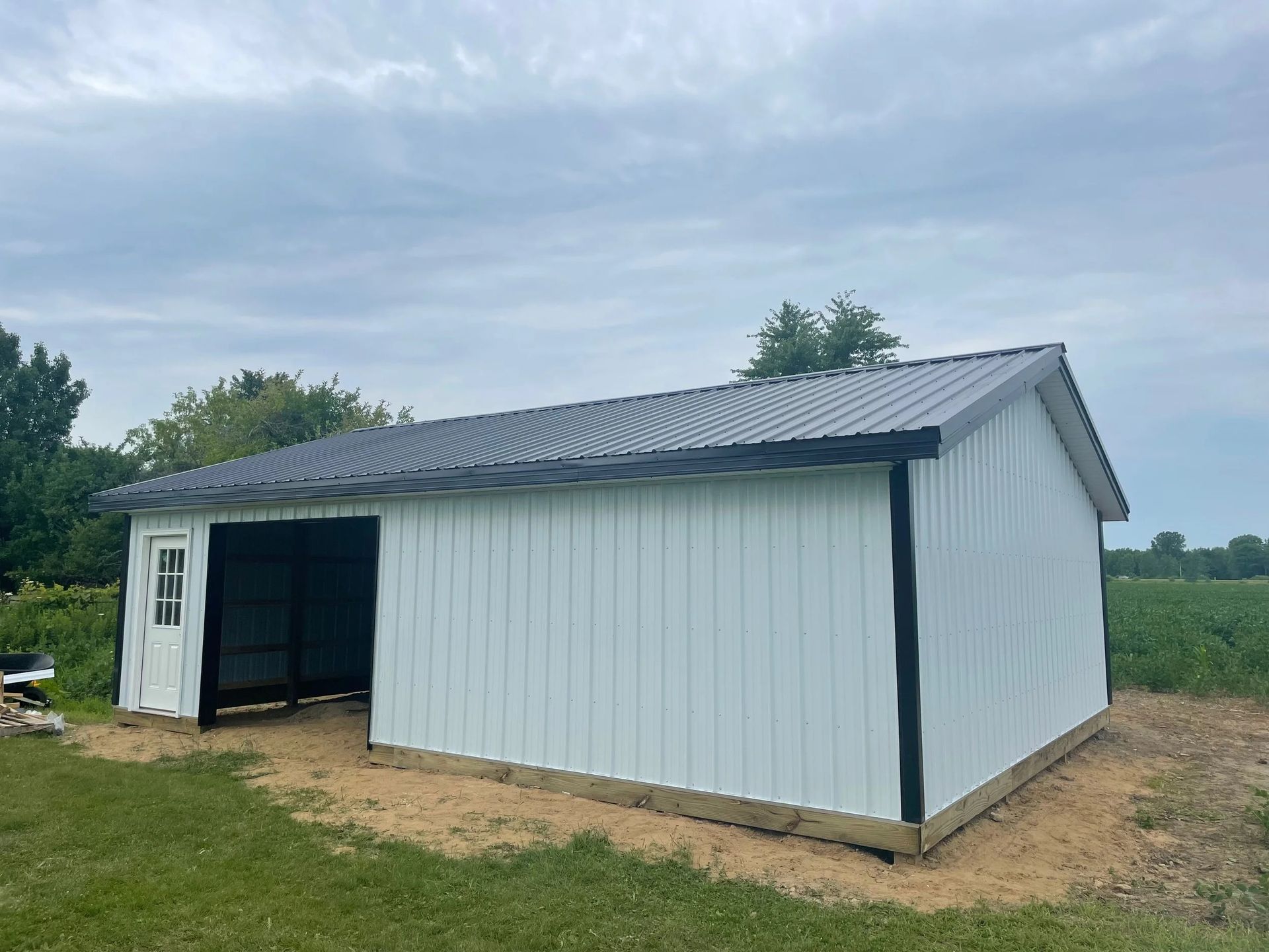 White metal barn-style shed with a gray roof and open doorway in a grassy field