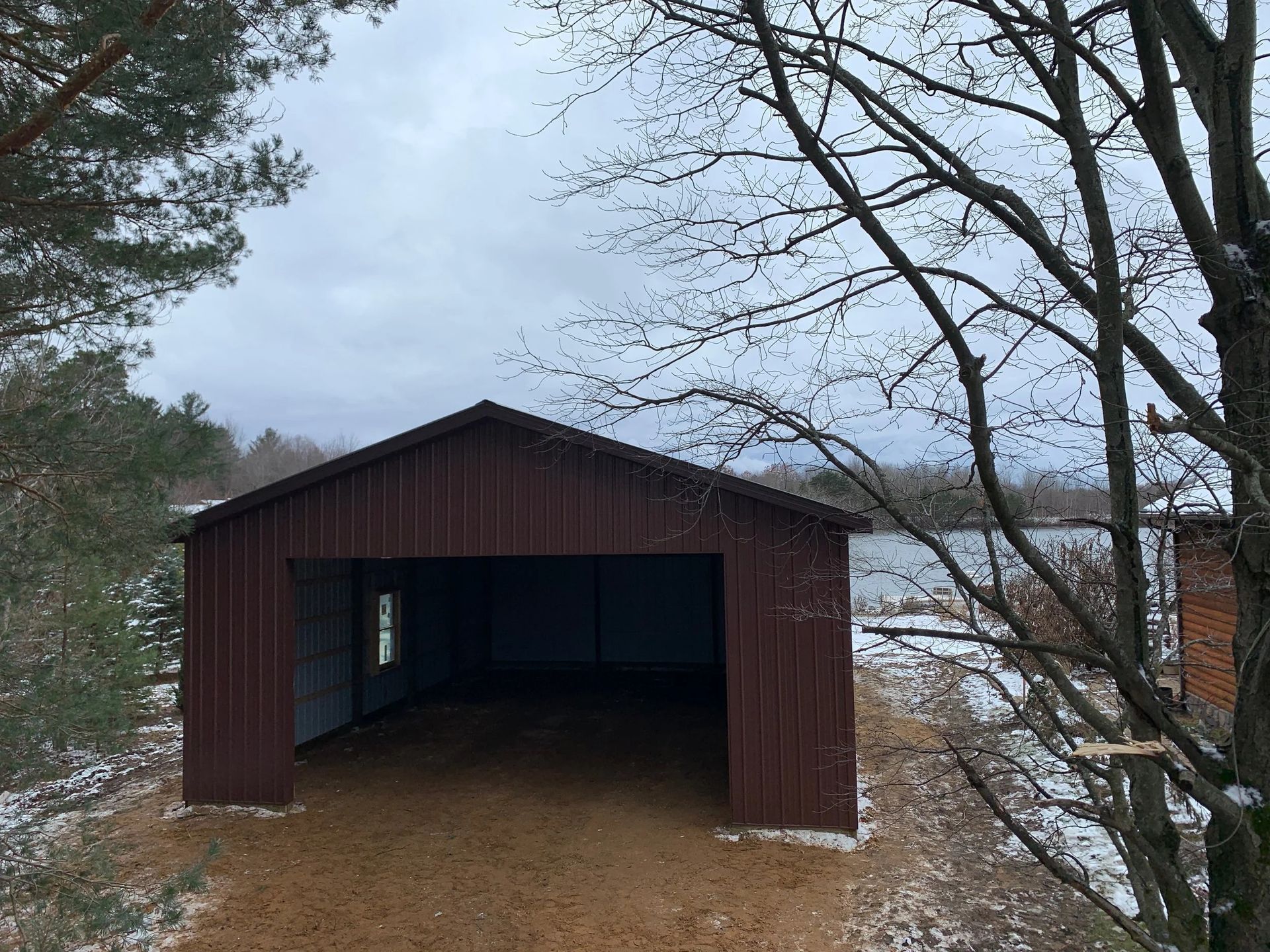 Brown wooden covered bridge over water, framed by leafless trees on an overcast day