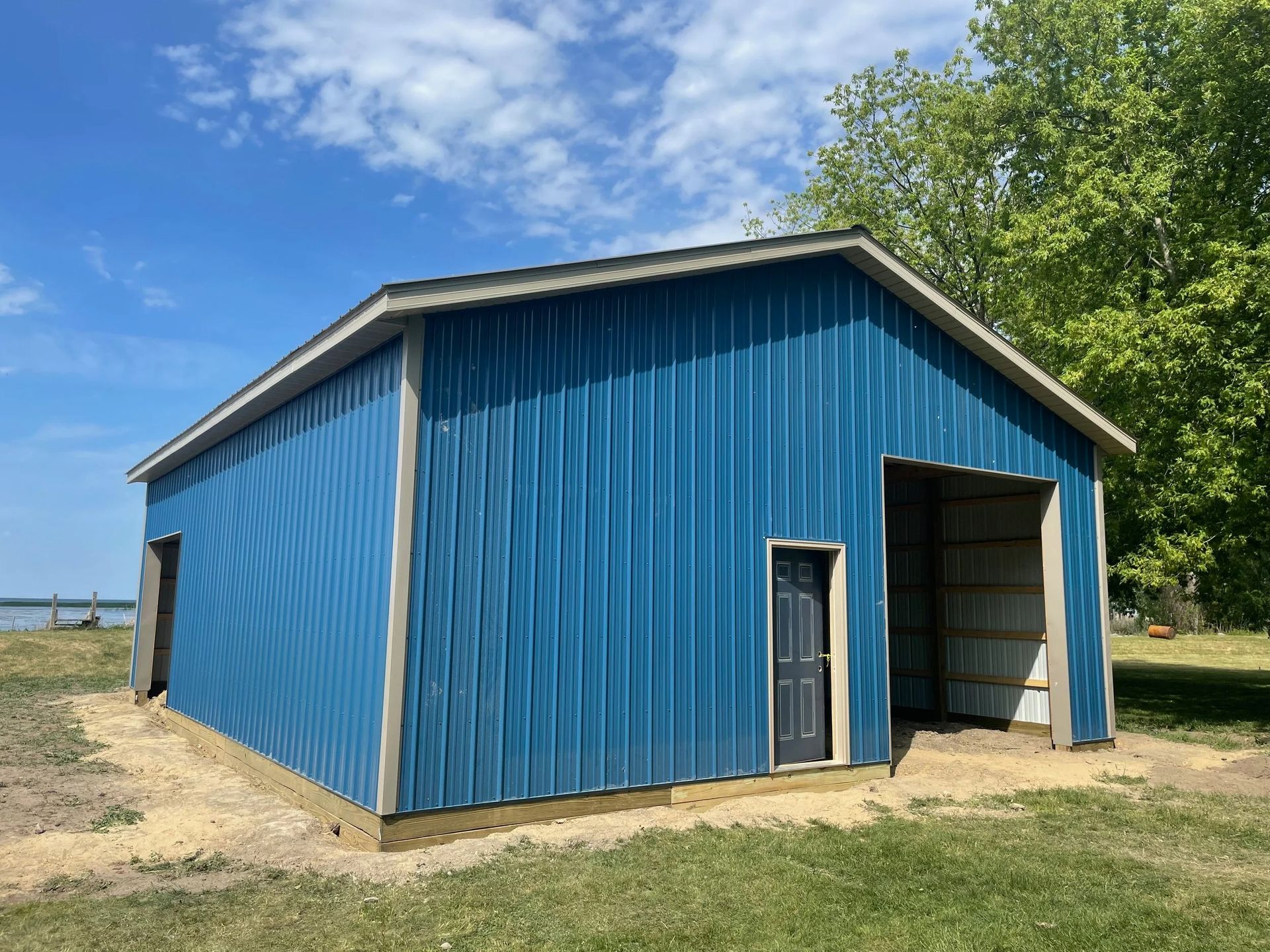 Blue metal barn with open doorway under a partly cloudy sky.