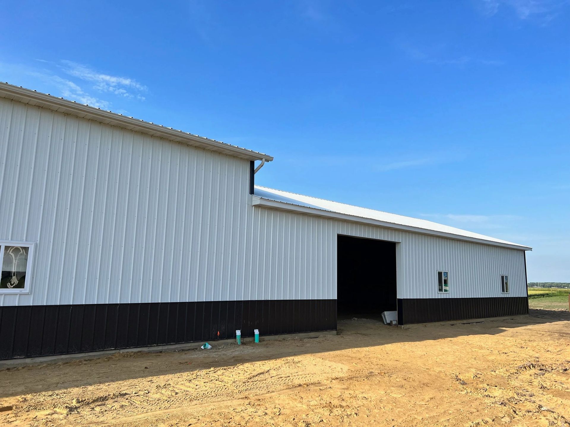 White metal barn with a large open doorway on a dirt lot under a clear blue sky.