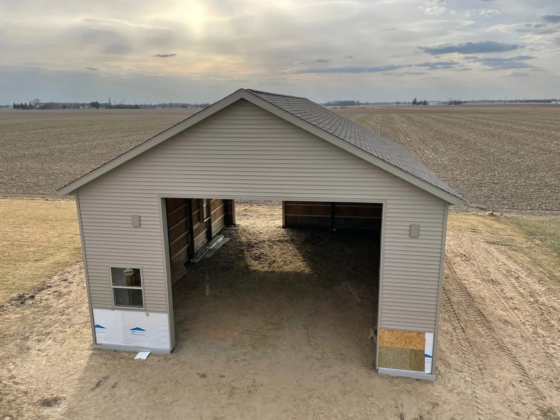Small tan shed with open front in a flat agricultural field under a cloudy sky.