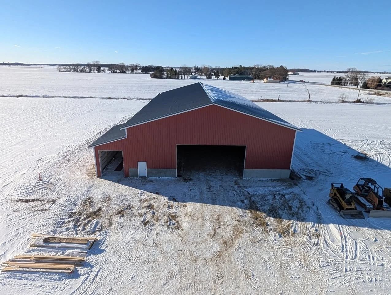 Red barn in a snowy field with farm equipment and open doors
