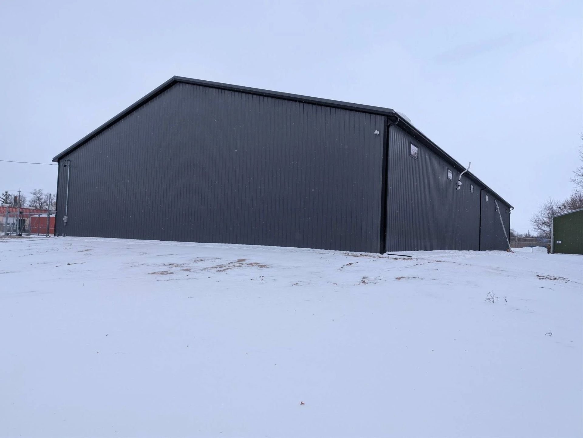 Dark gray metal barn on a snowy field under an overcast sky