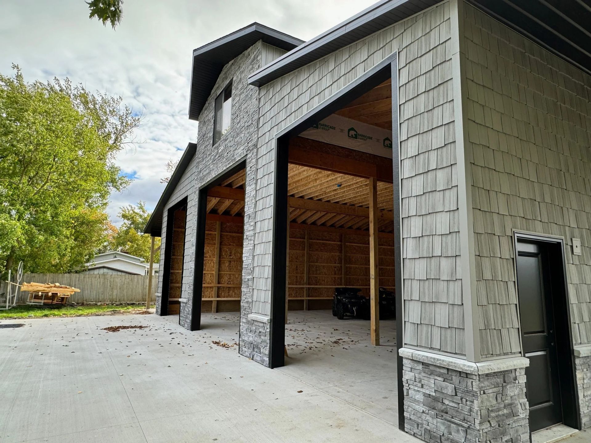 New gray-sided garage with open bays and unfinished wood interior beside a paved driveway