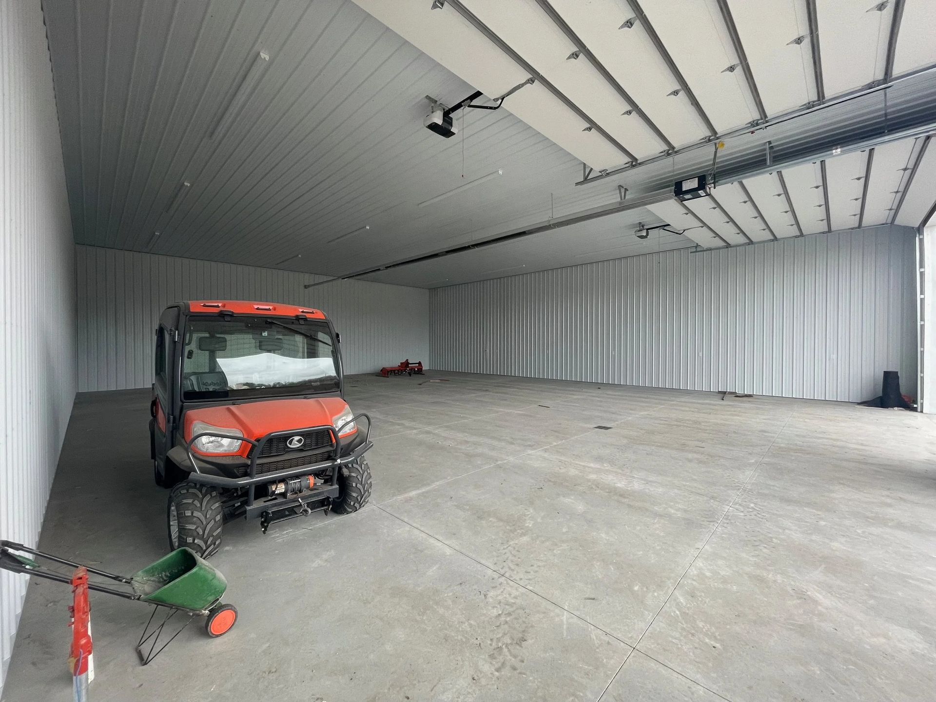 Red utility vehicle parked inside a large empty metal warehouse with concrete floor.