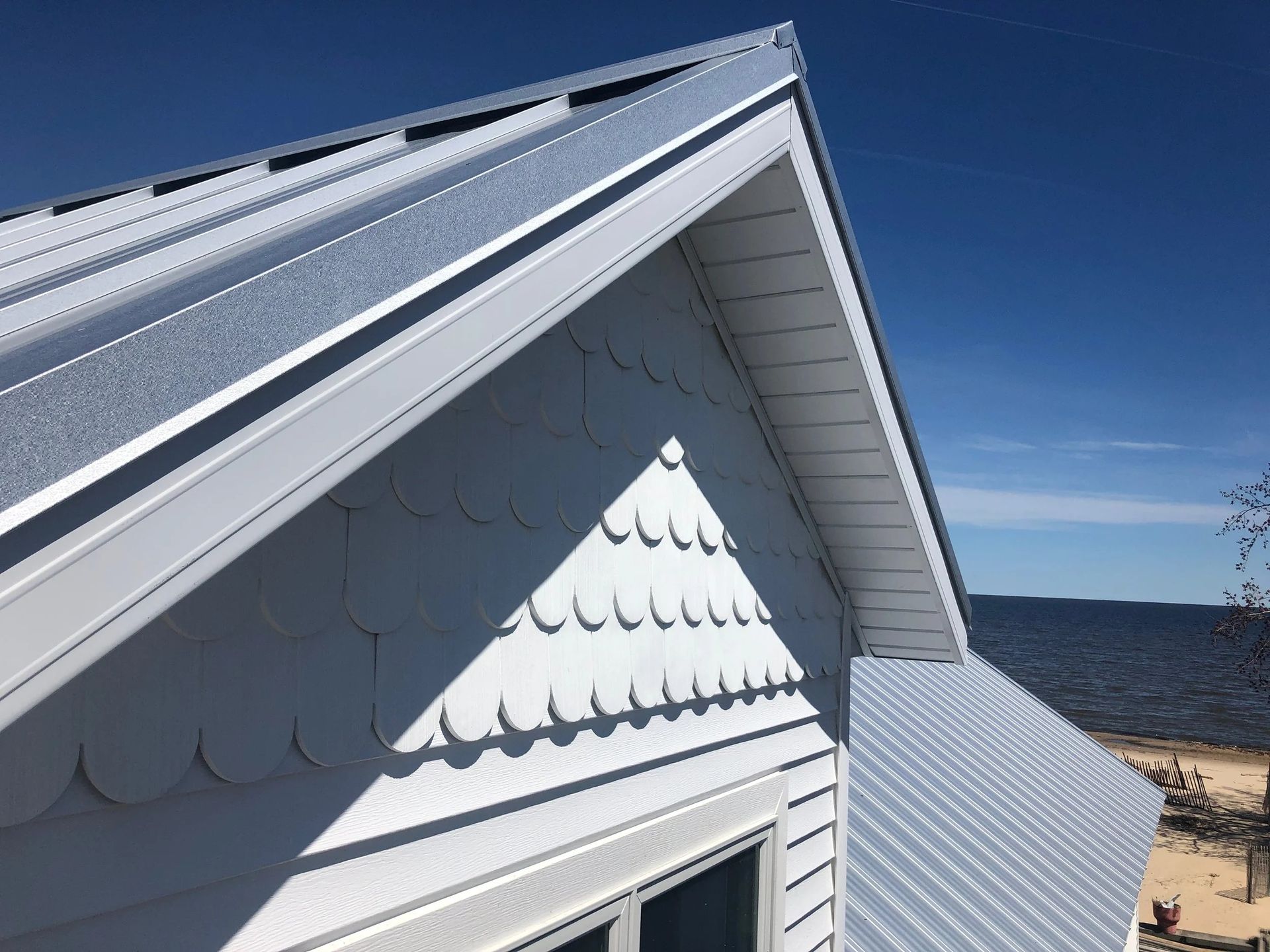 White house roof with dormer and shingles overlooking a blue ocean under a clear sky