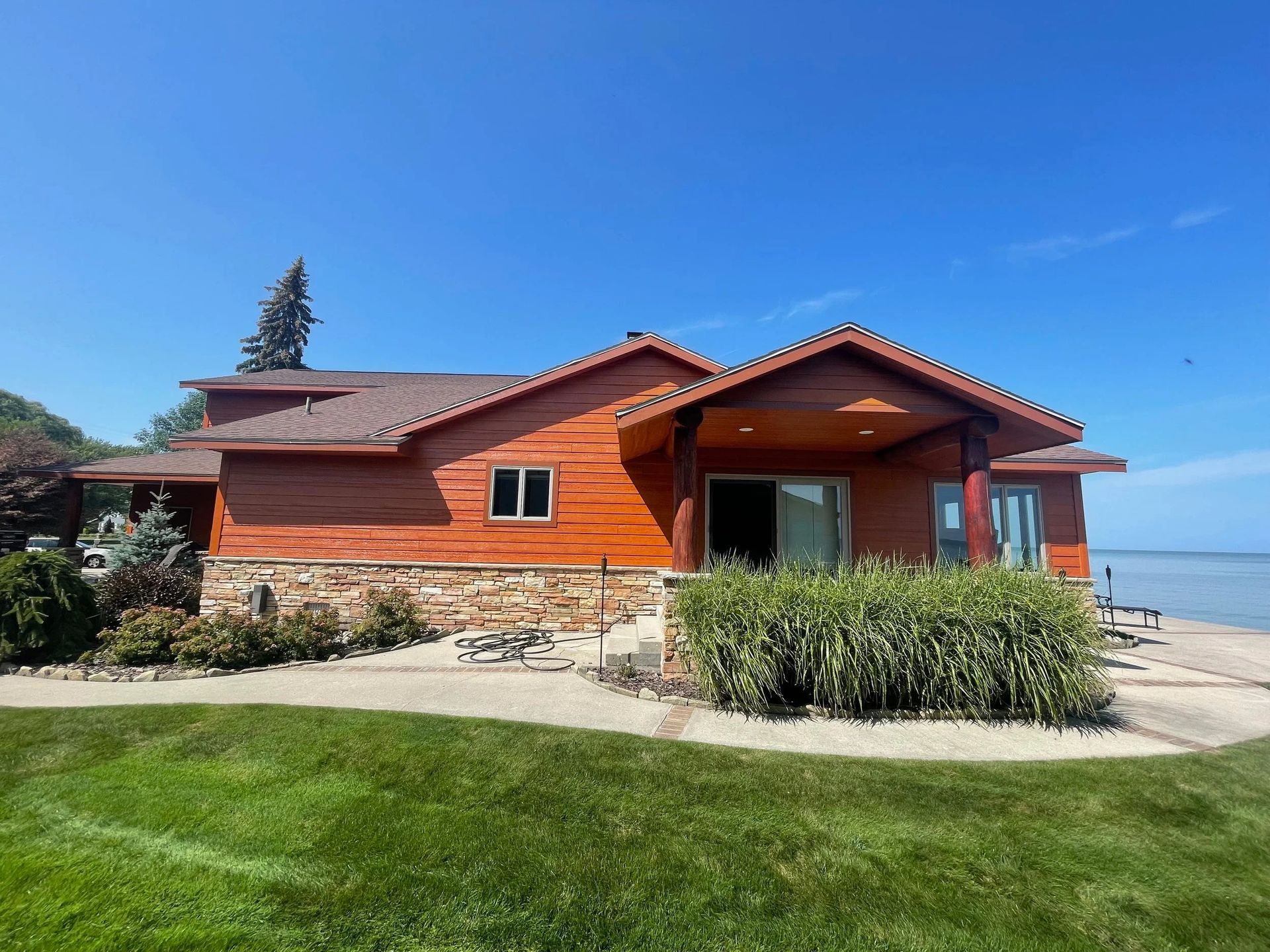 Orange lakeside house with stone foundation, green lawn, and blue sky
