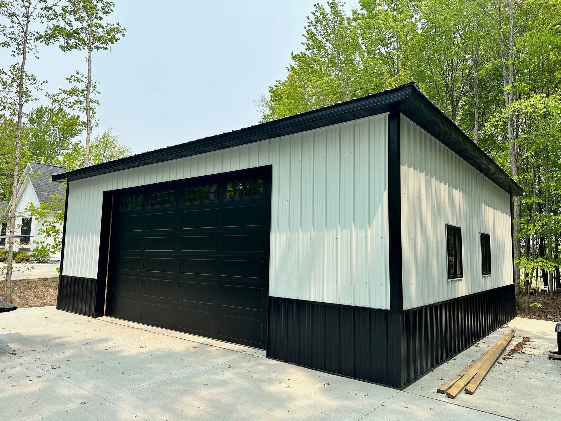 White-and-black detached garage with large black door in a wooded yard under construction